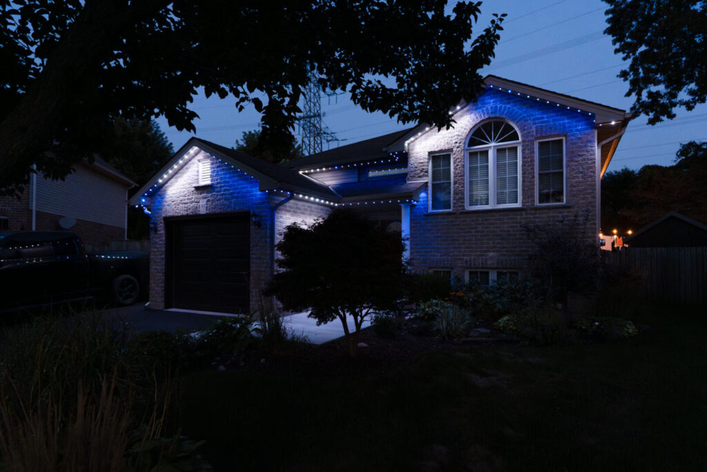 Blue permanent lighting on a brick raised bungalow at dusk