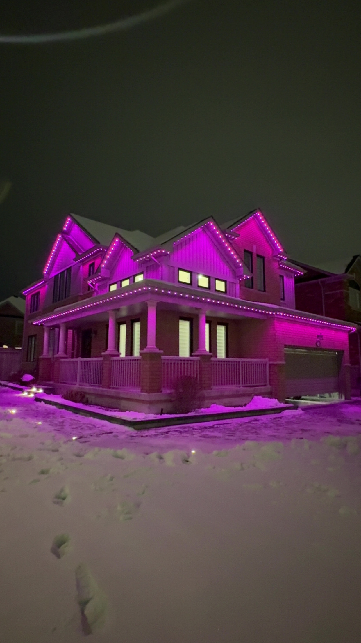 Magenta permanent lighting on a brick home with a wraparound porch in snow