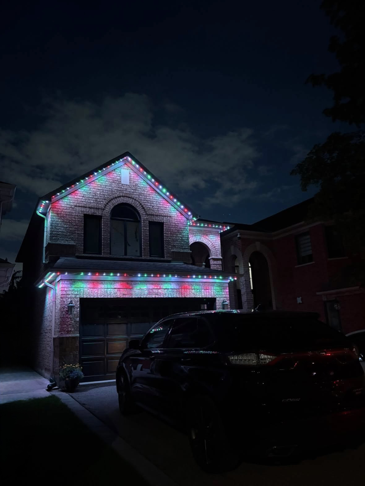 Red, green and teal permanent lighting on a brick home with an arched window