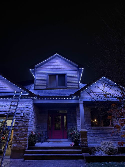 Cool white and blue permanent lighting on a stone home with a red door