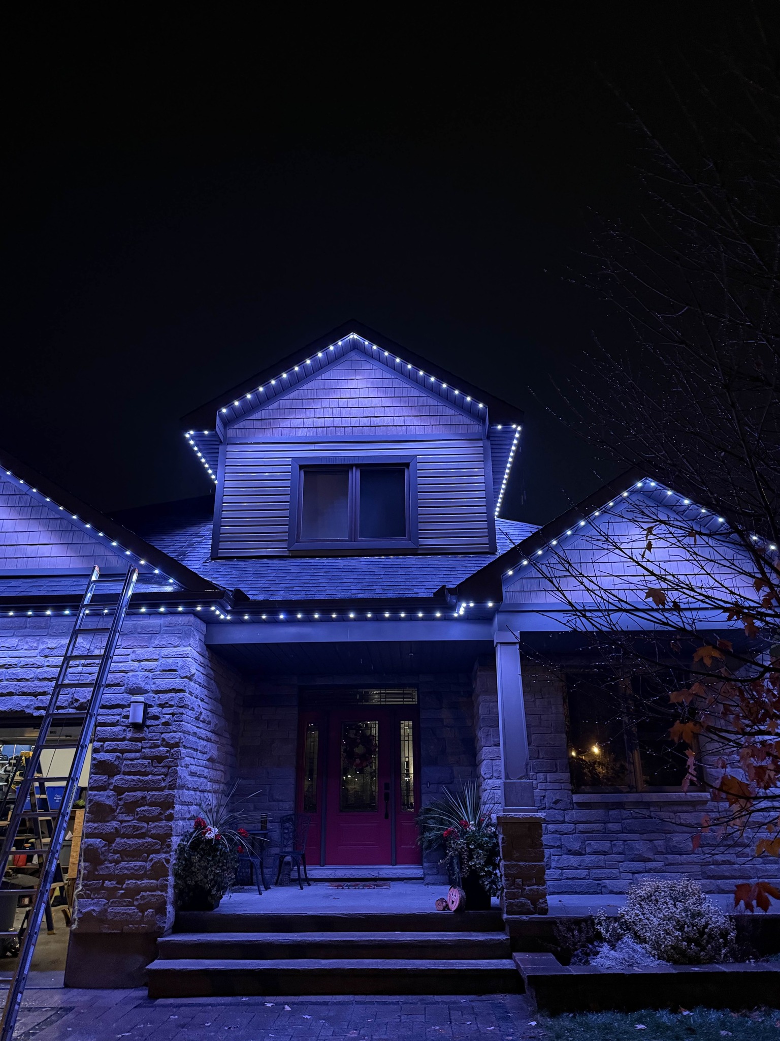 Cool white and blue permanent lighting on a stone home with a red door