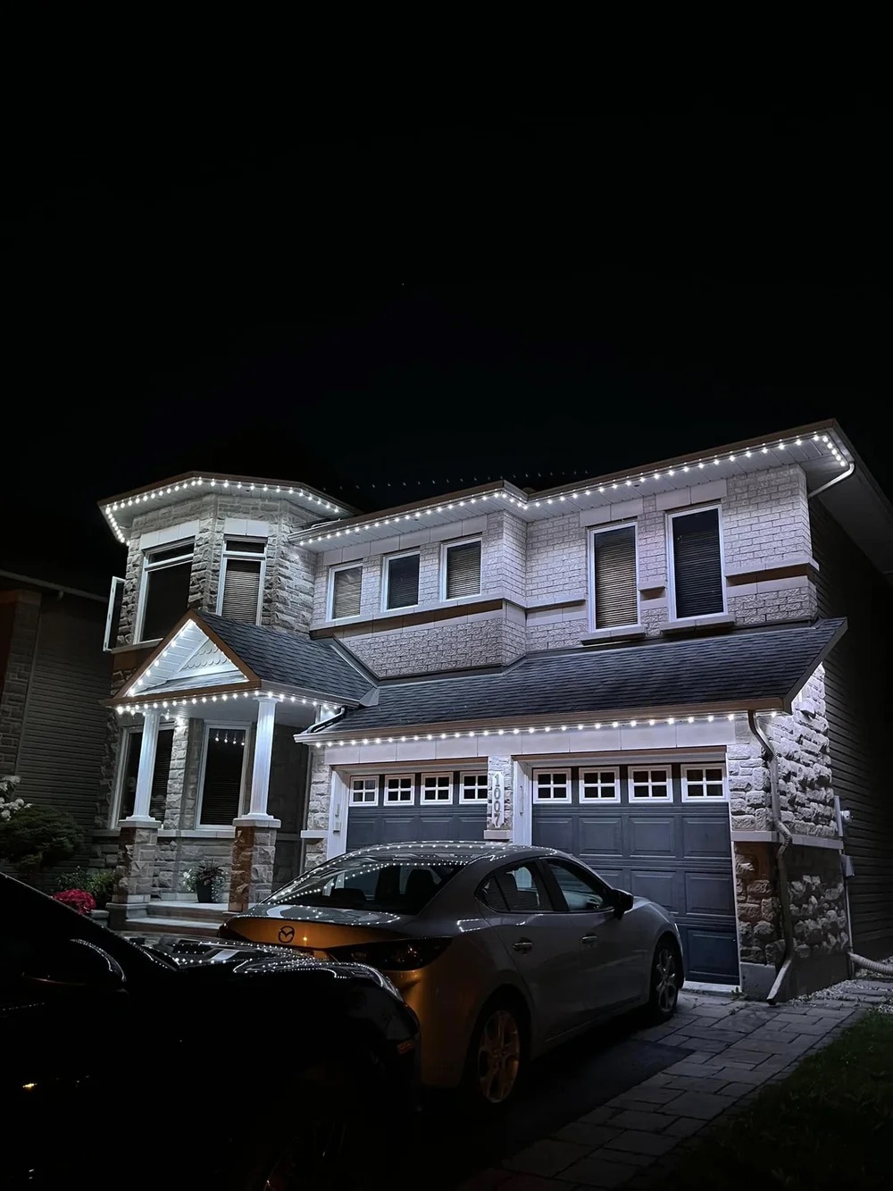 White permanent lighting on a stone and brick home