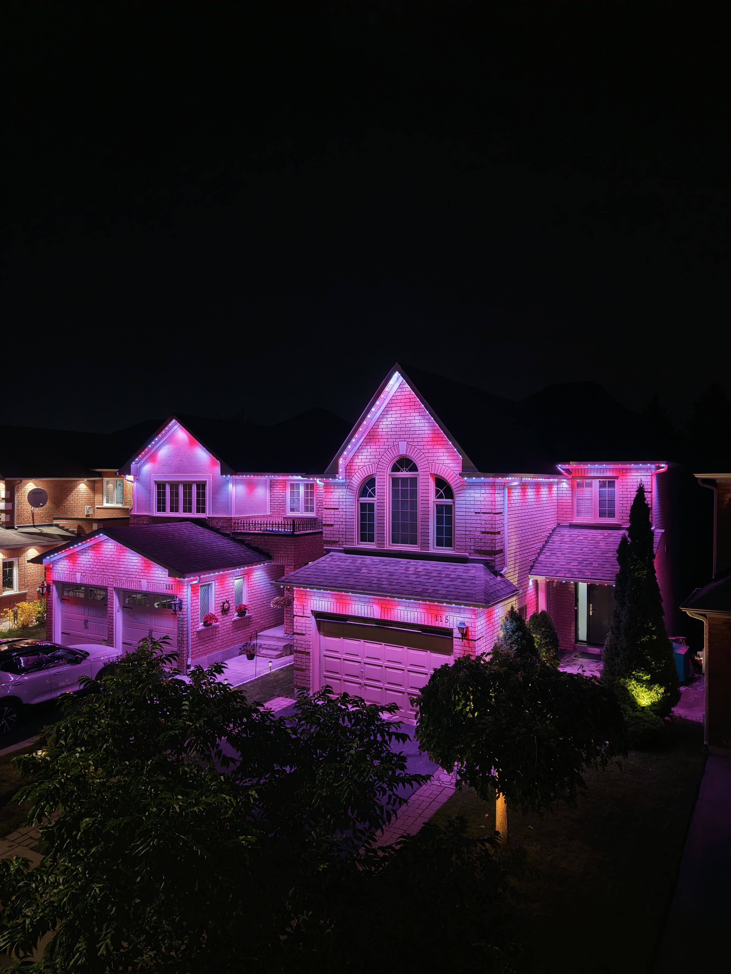 Pink and white permanent lighting on a two-storey brick home