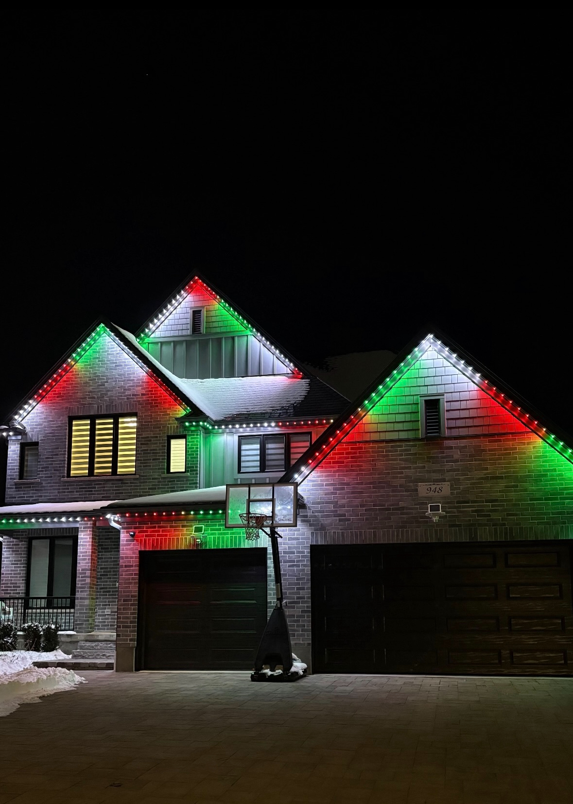 Red and green permanent Christmas lighting on a brick home in winter