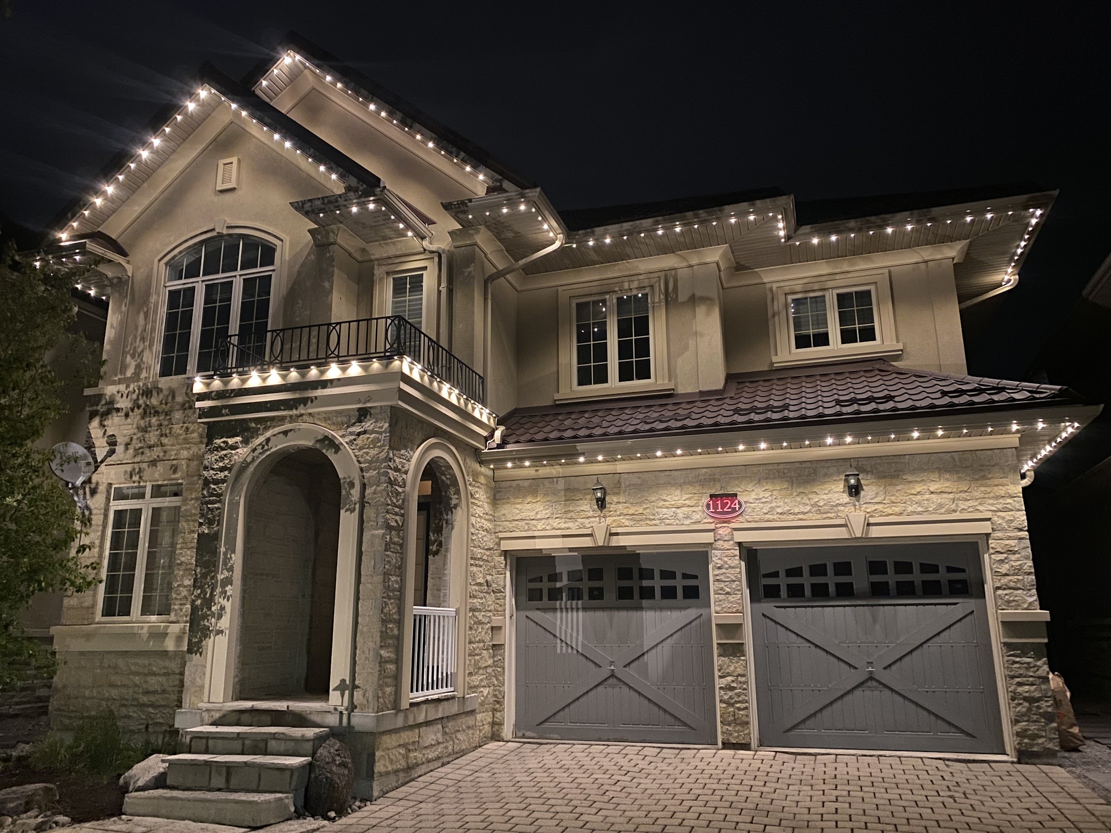 Warm white permanent lighting on a large stone and stucco home