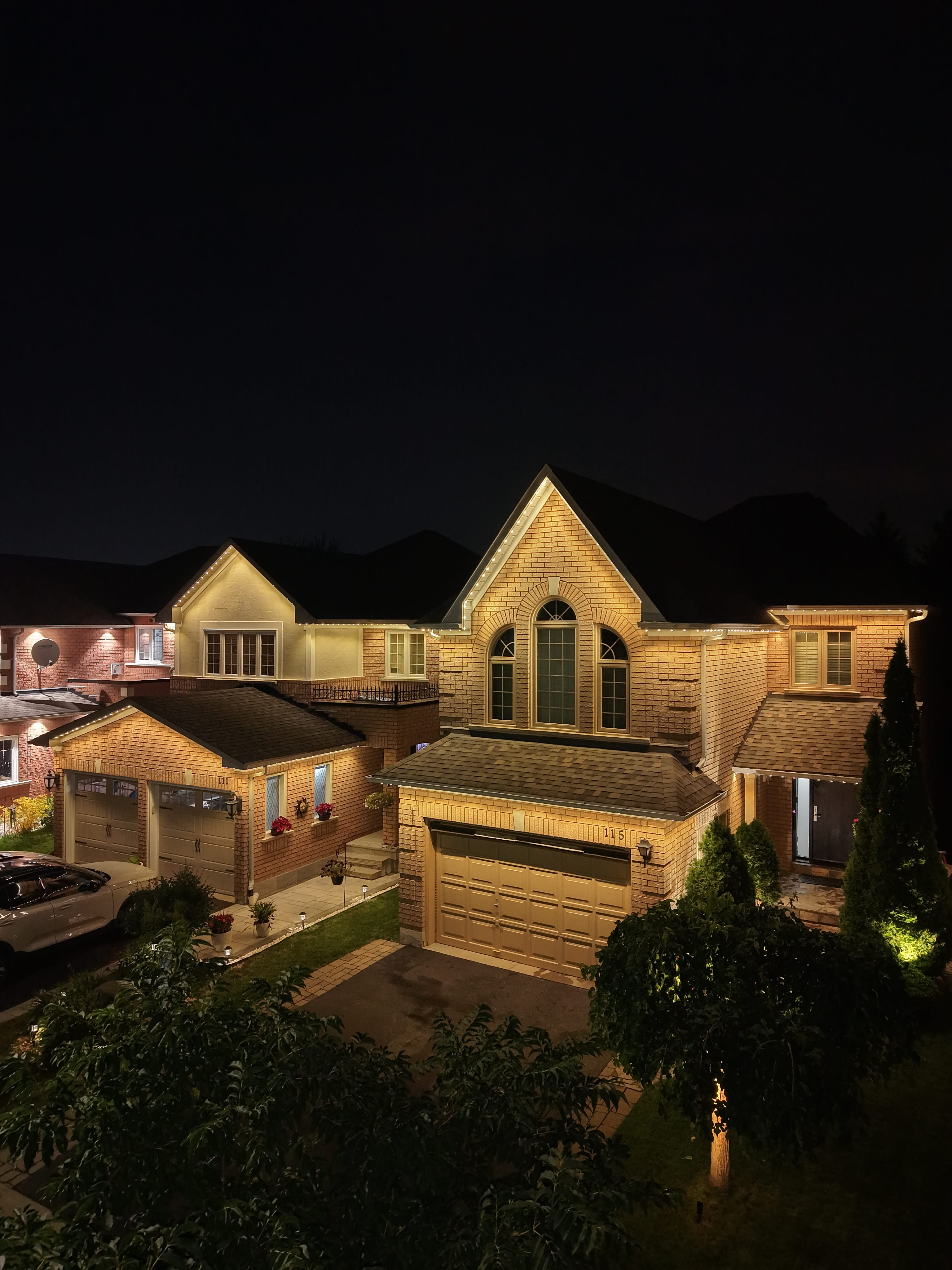 Warm white permanent lighting on a two-storey brick home at night
