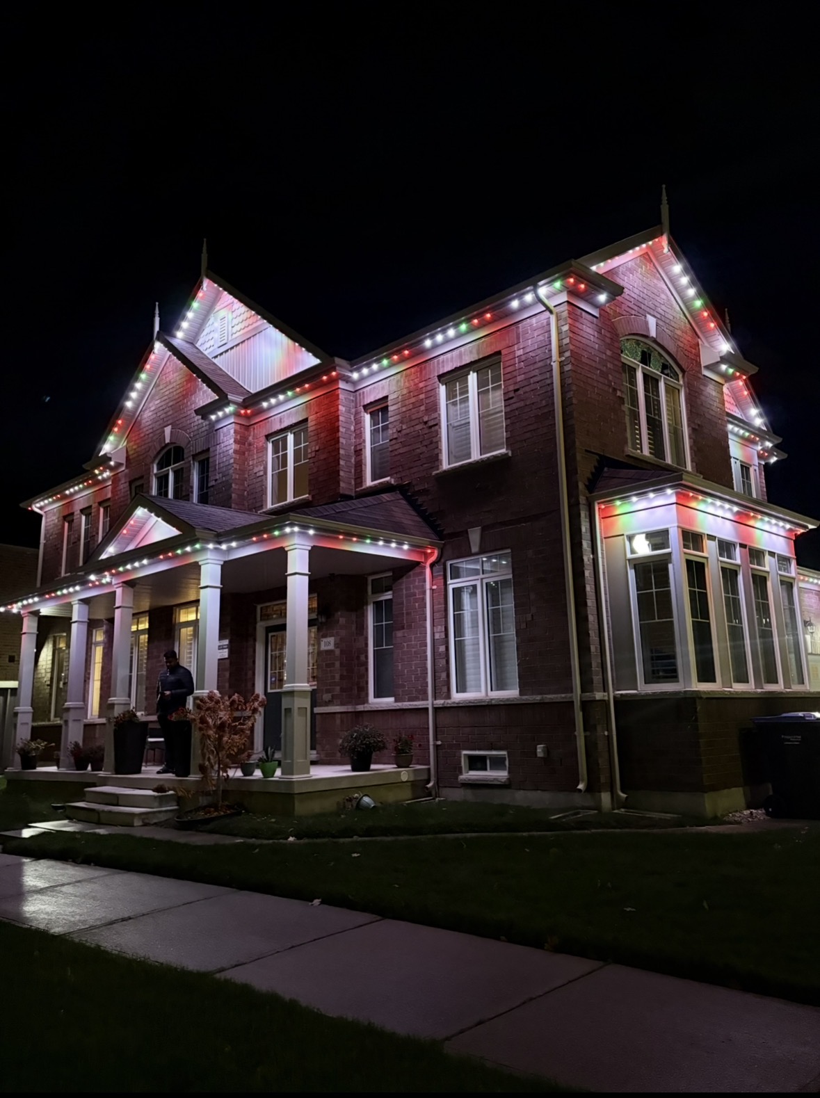 Red and green permanent Christmas lighting on a red-brick home with a porch