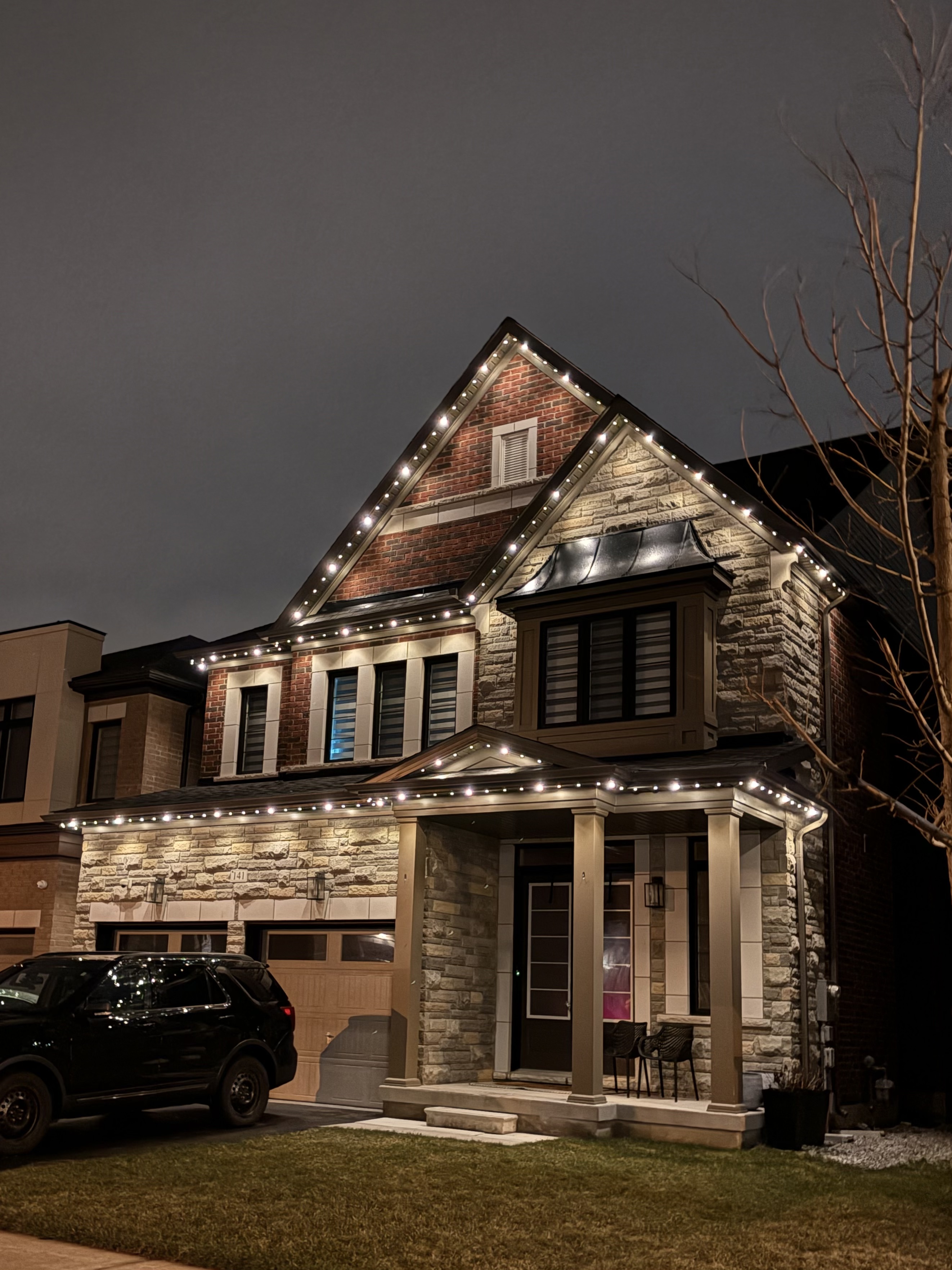 White permanent lighting on a stone and brick two-storey home