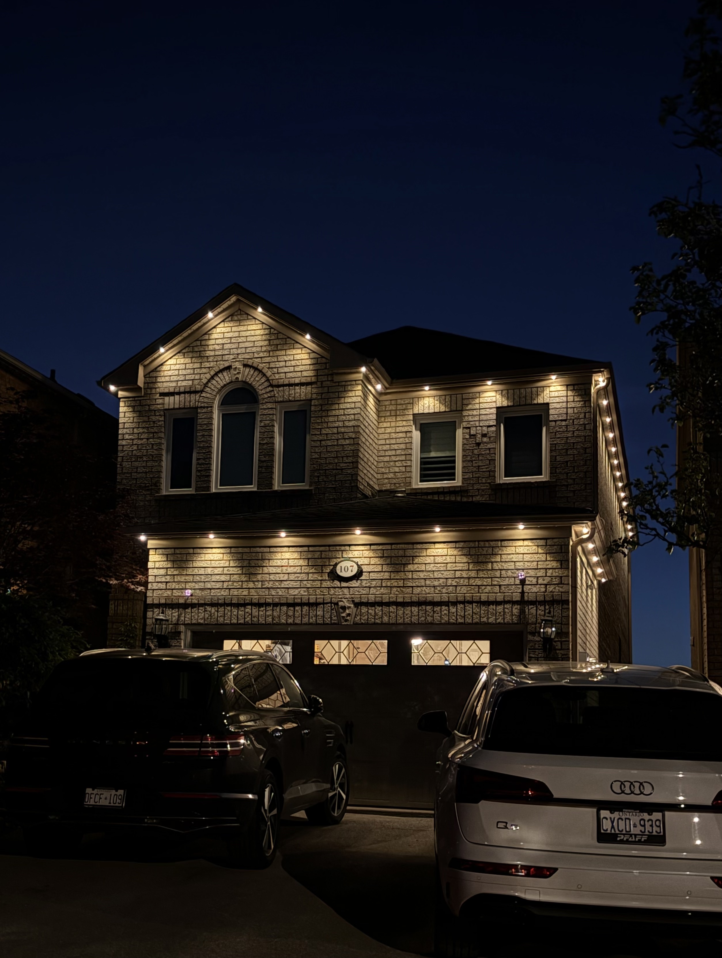 Warm white pot-light style permanent lighting under the soffit of a brick home