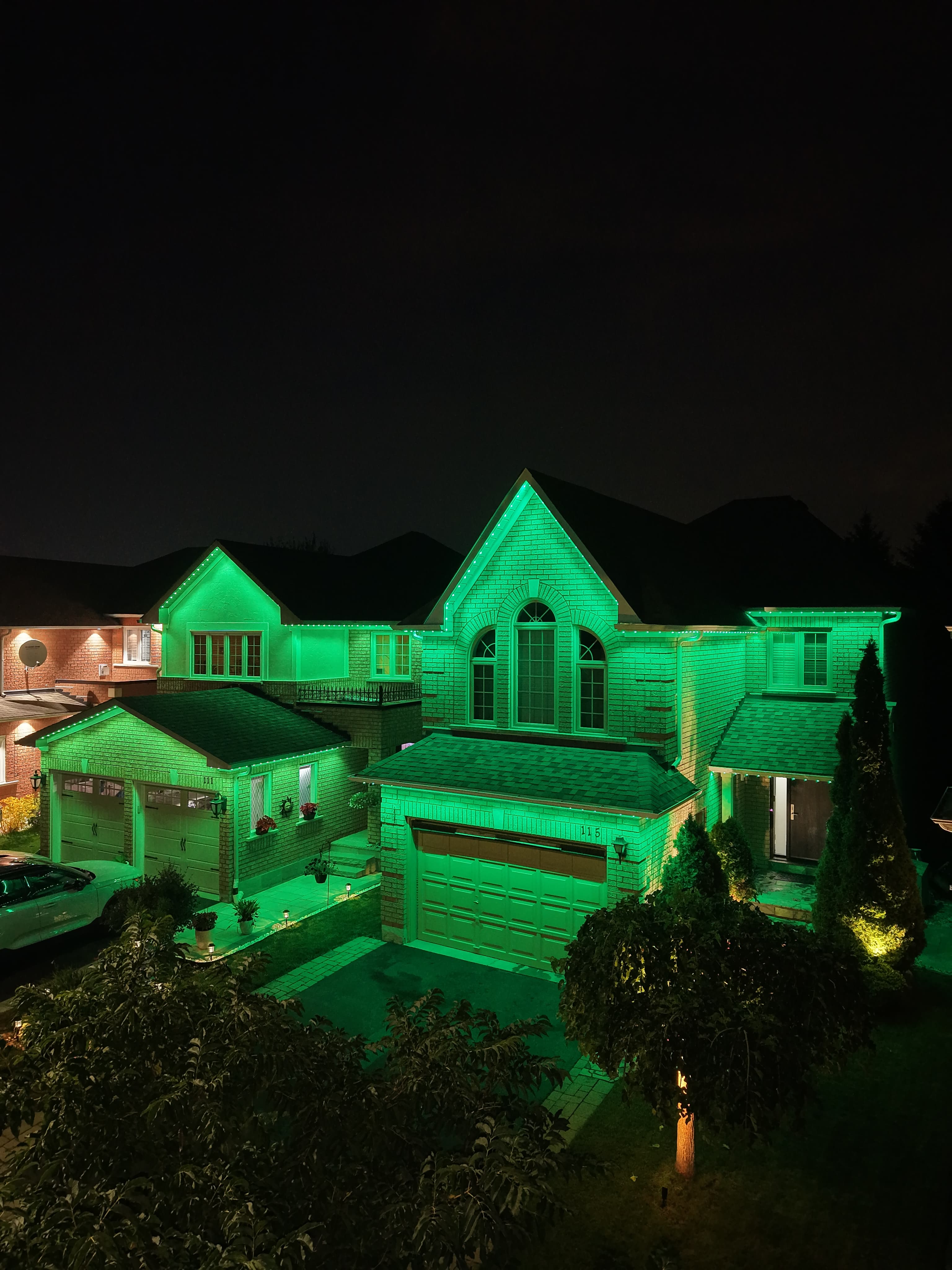 Green permanent exterior lighting on a two-storey brick home at night