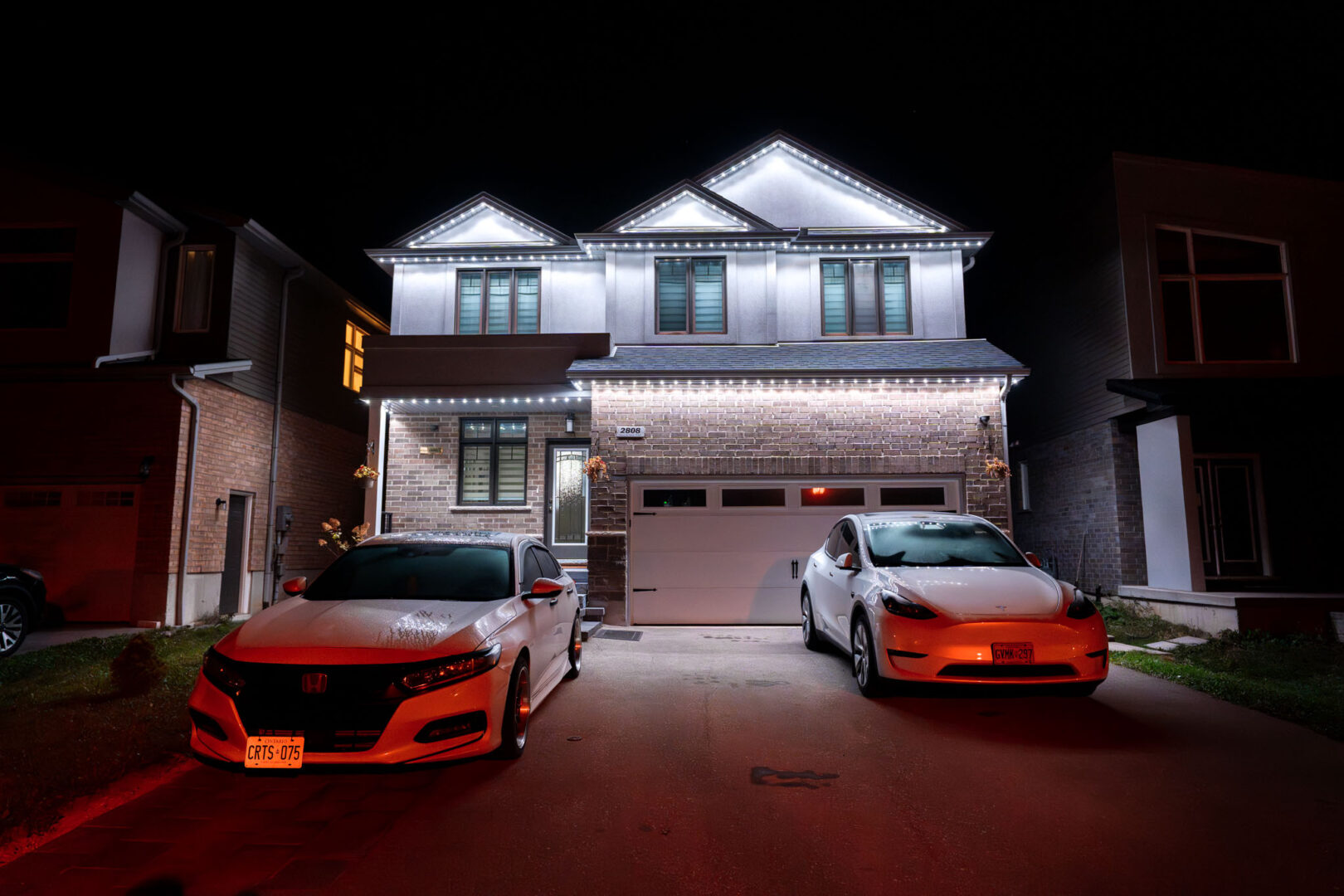 White permanent lighting on a two-storey home with cars in the driveway