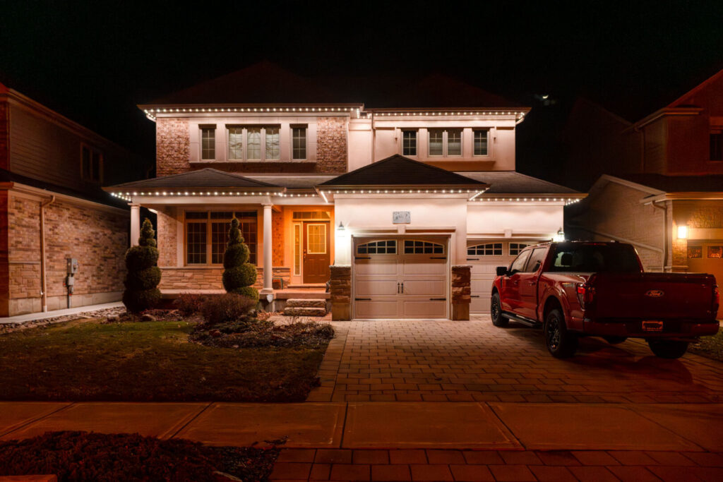 Warm white permanent lighting on a brick home with a red truck
