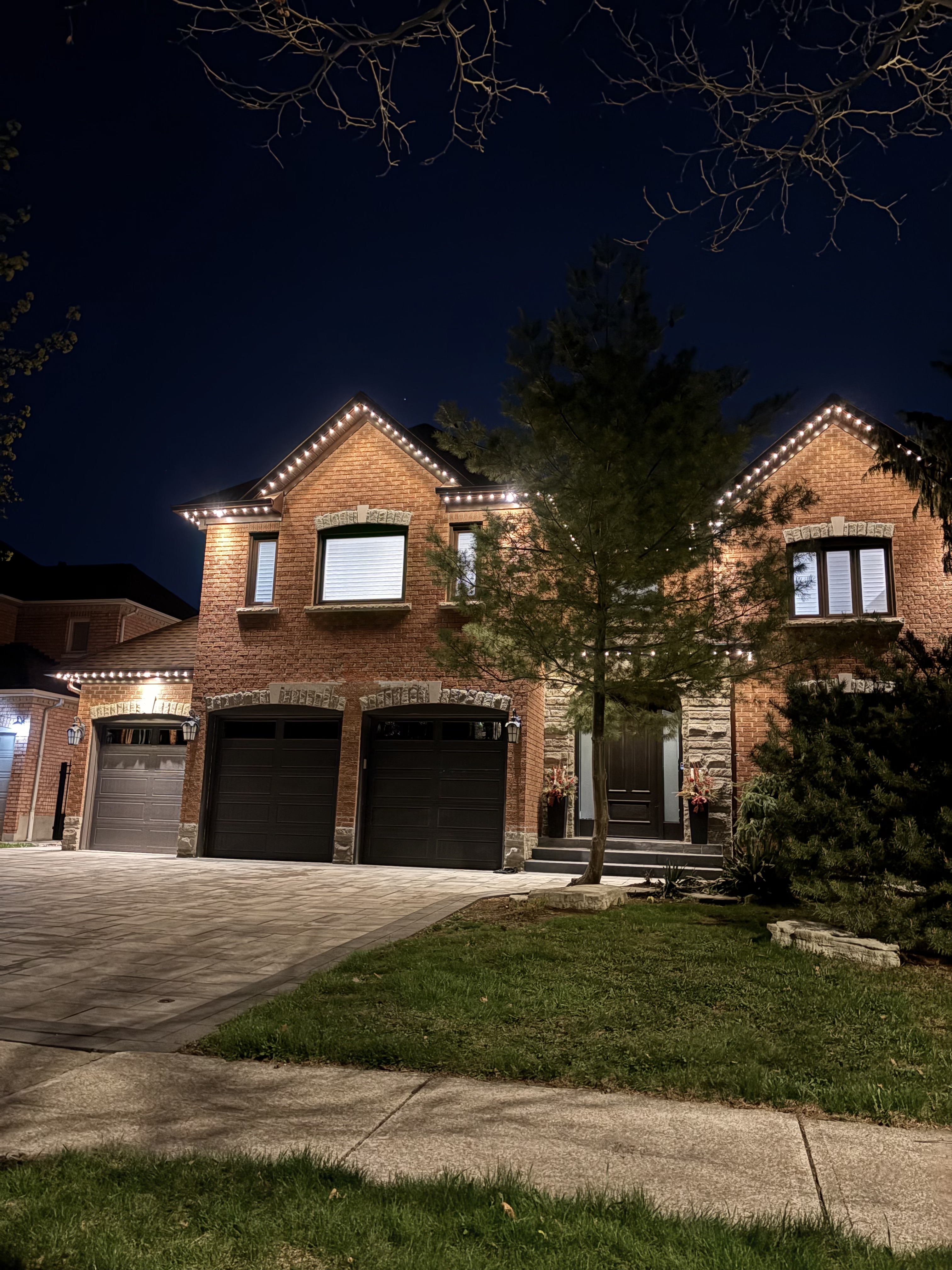 Warm white permanent lighting on a brick two-storey home at night
