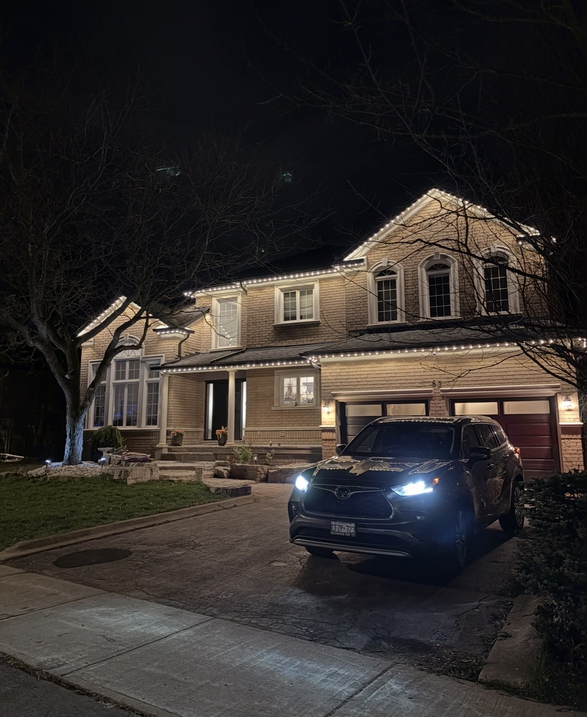 Warm white permanent lighting on a beige brick two-storey home