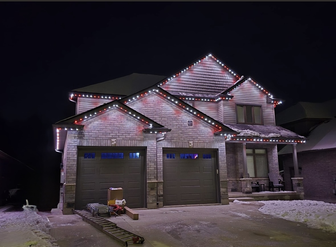 Red and white permanent lighting on a brick home in snow