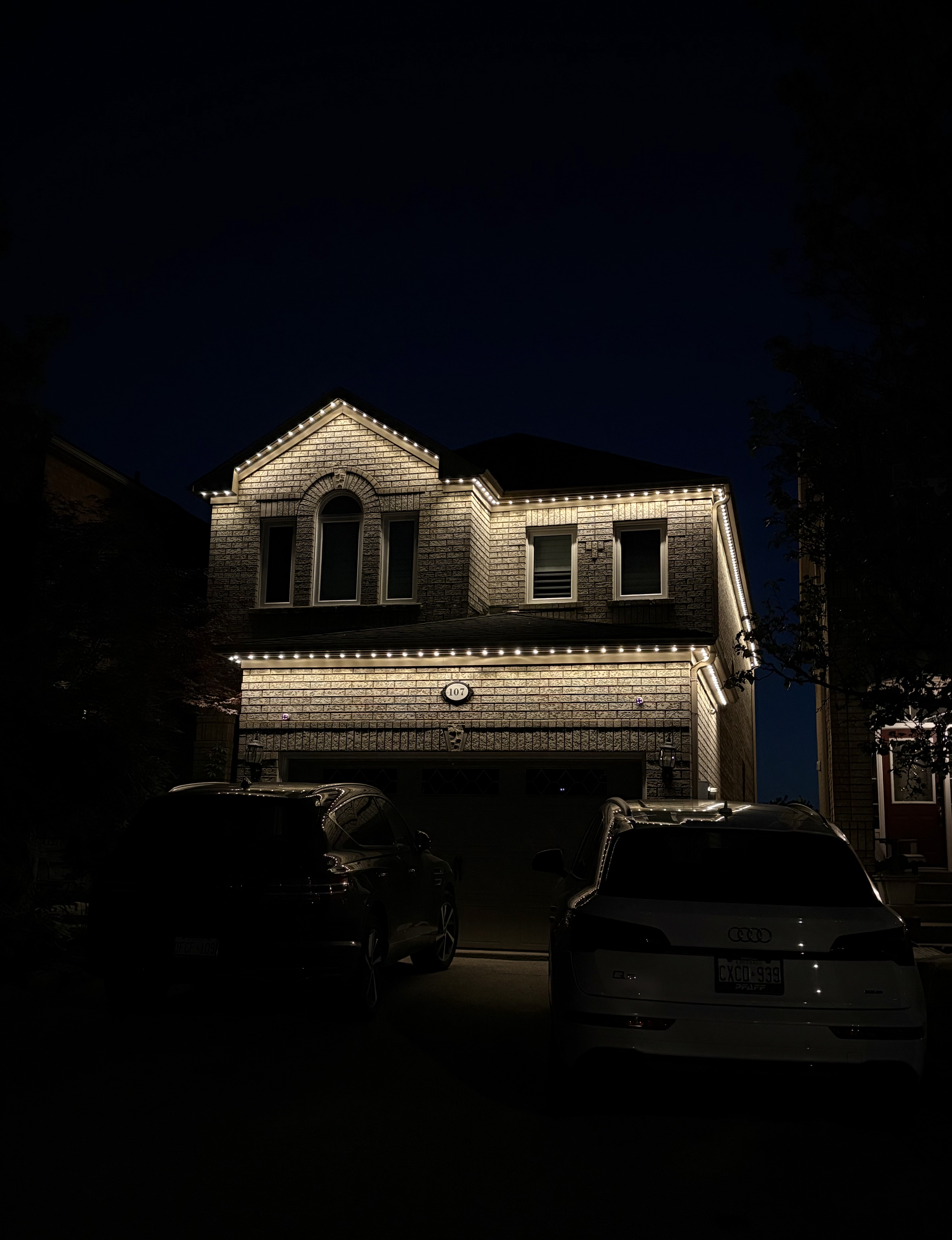 Warm white permanent roofline lighting on a brick home at dusk