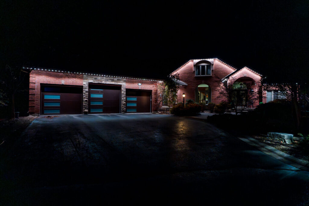 Permanent lighting on a wide brick home with a three-car garage