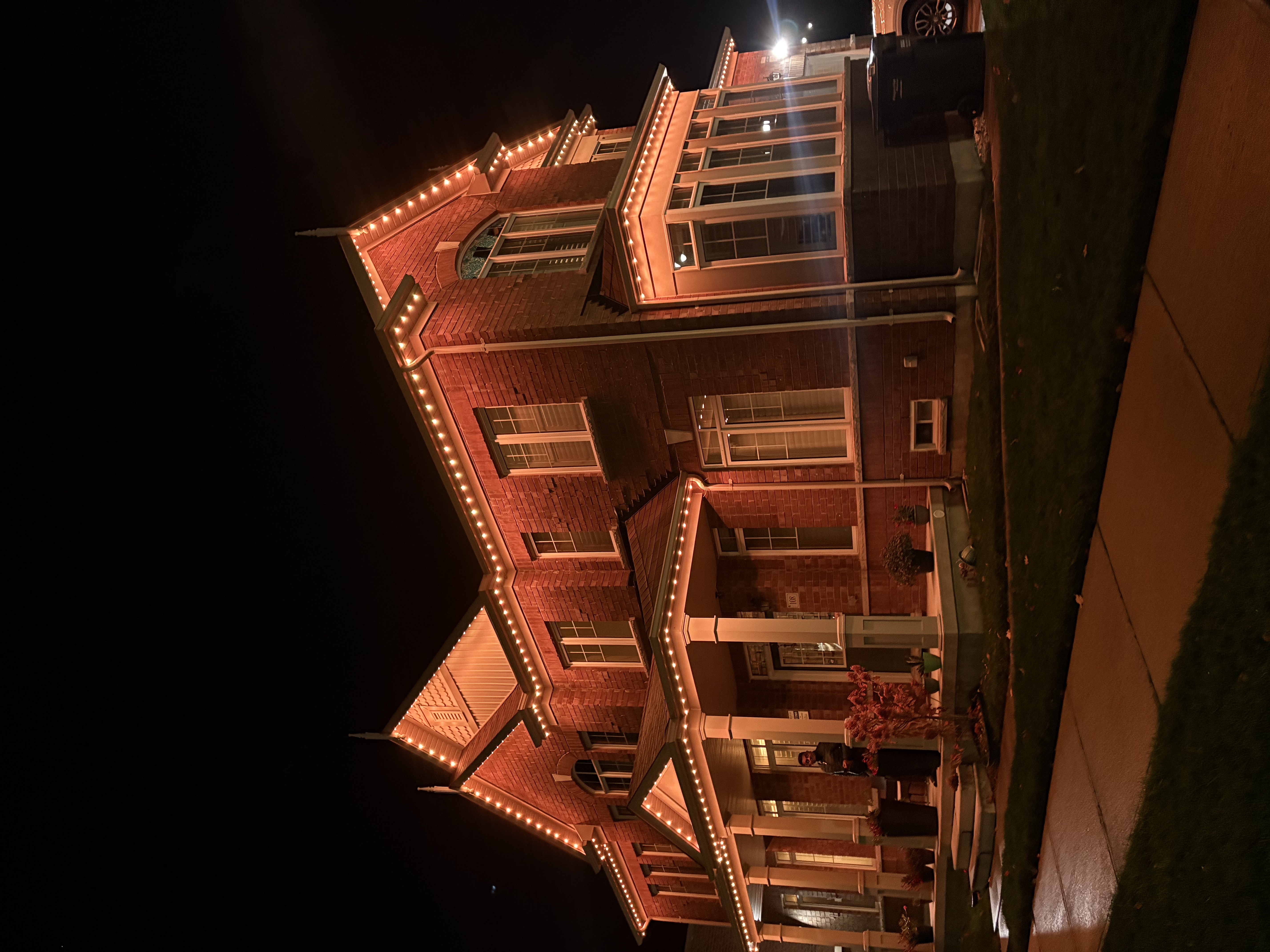 Warm white permanent lighting on a large red-brick home