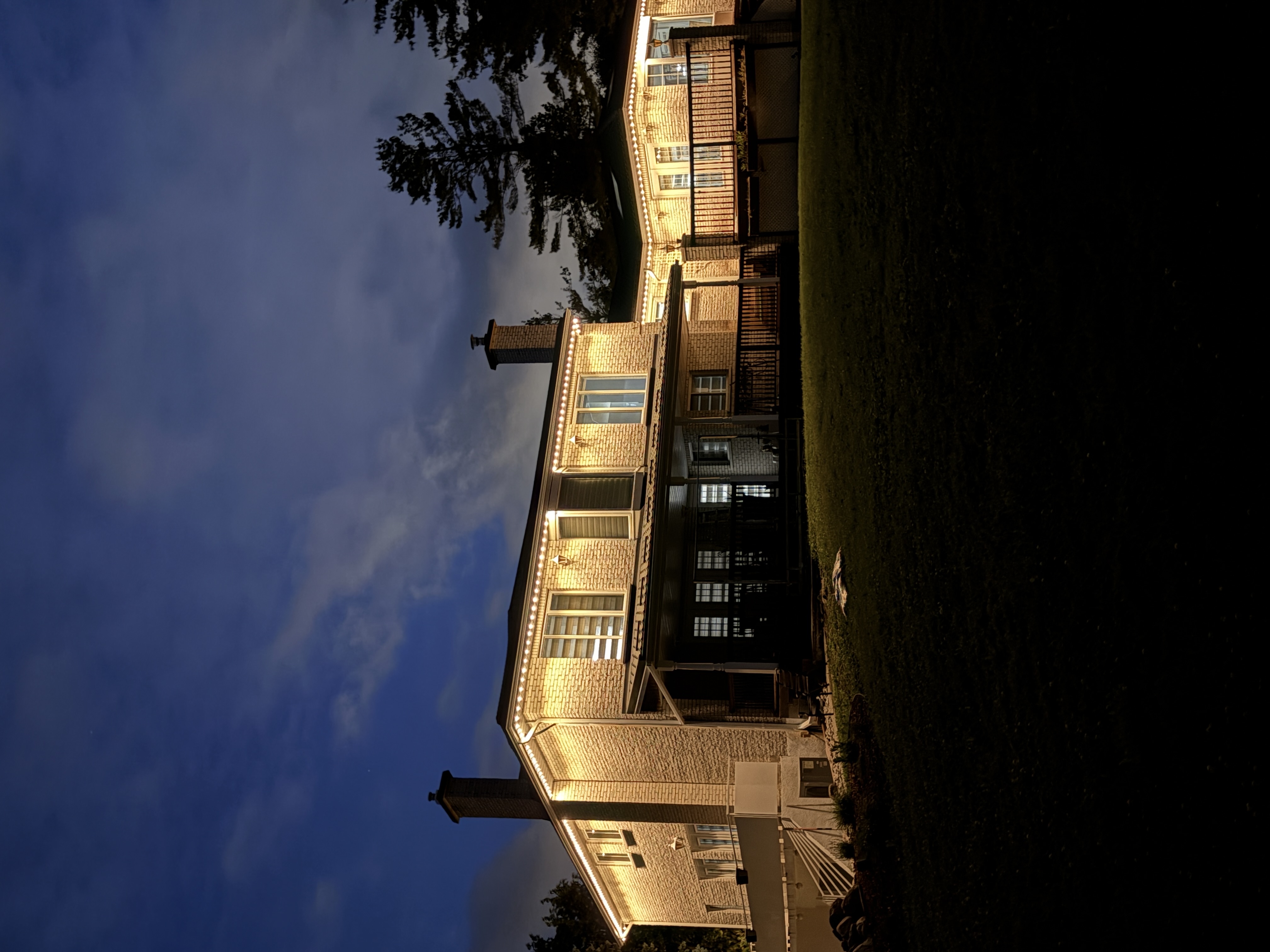 Warm white permanent lighting on a large home with chimneys