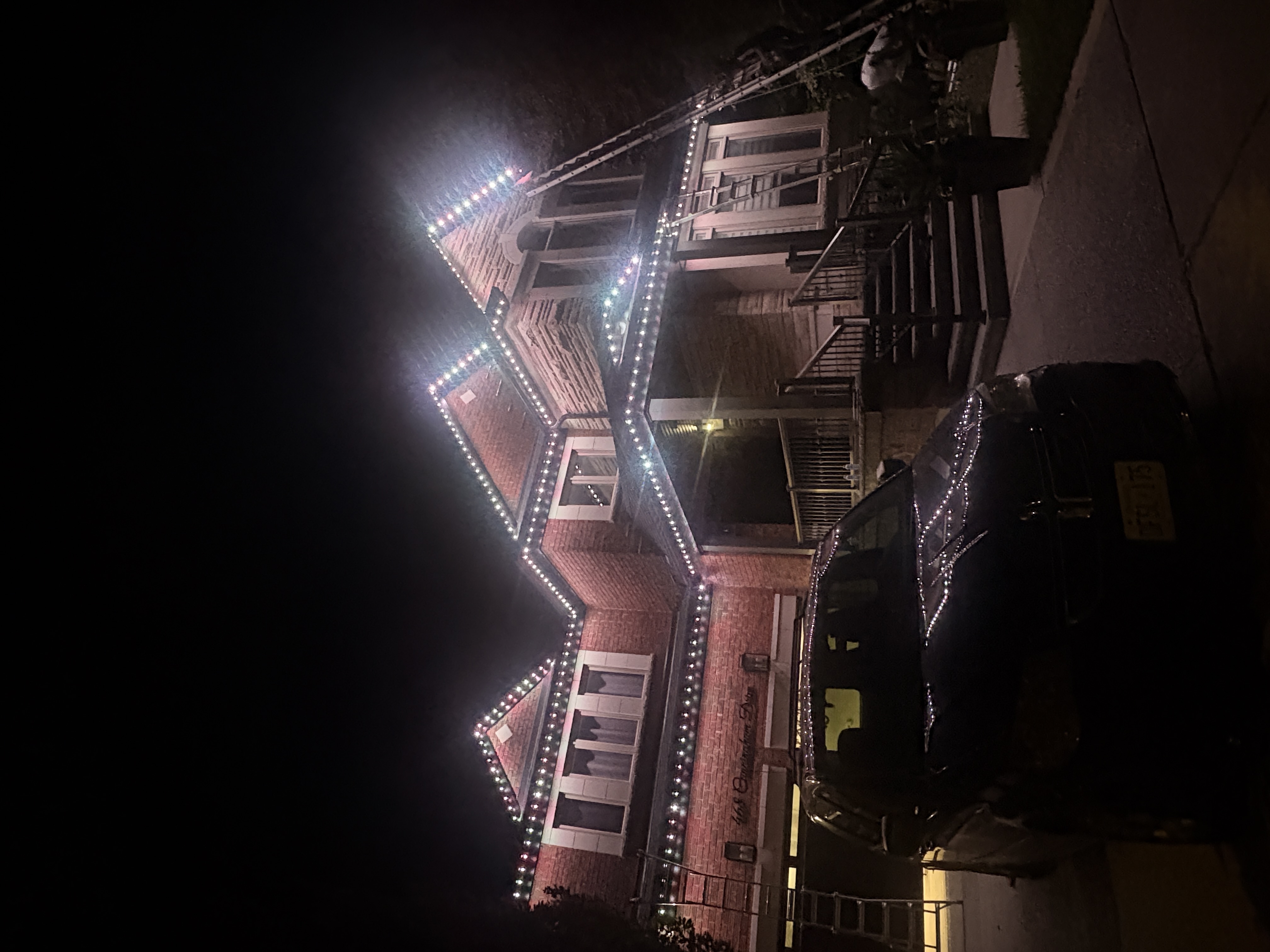 White permanent lighting on a red-brick home with porch stairs