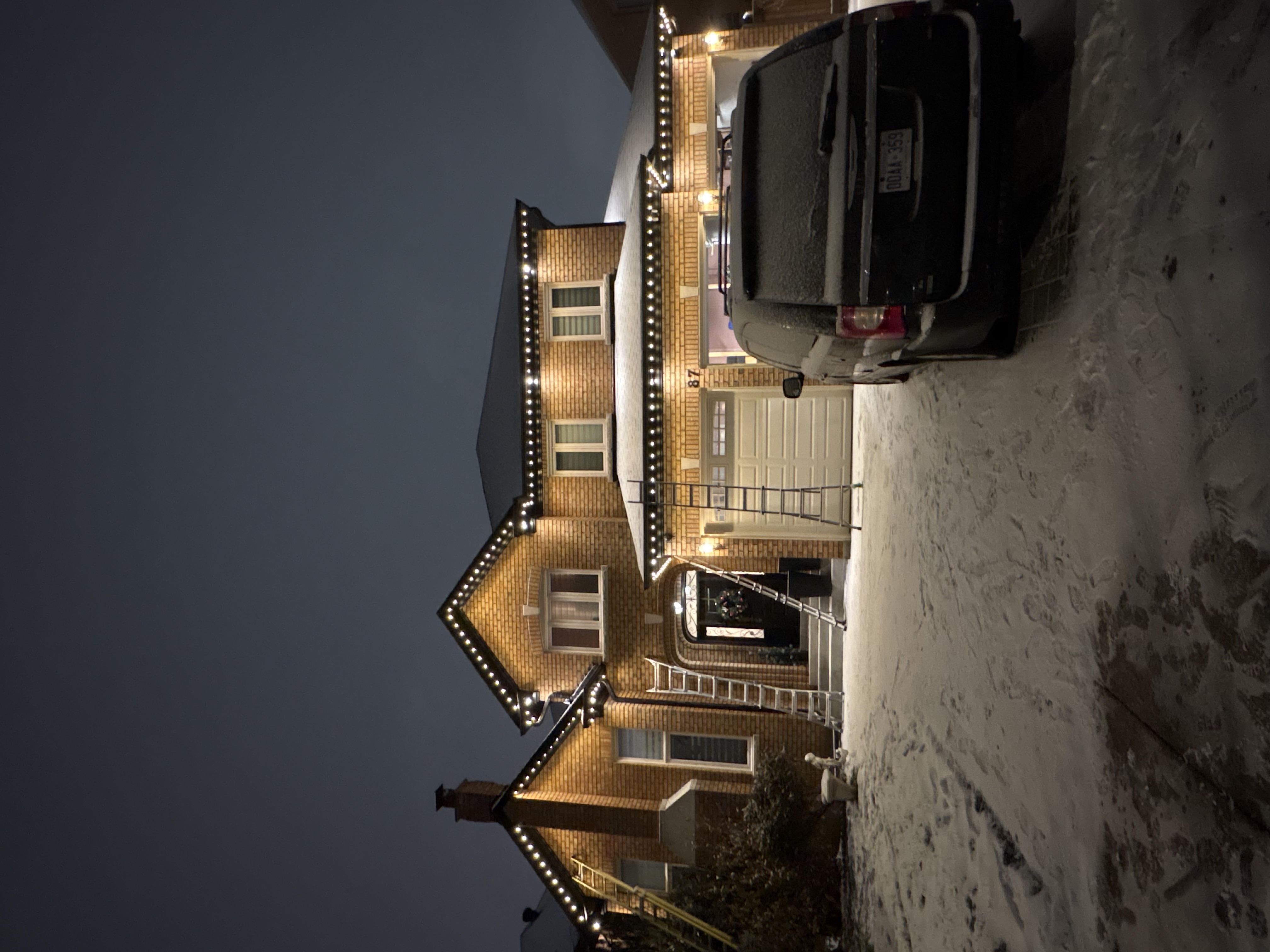 Warm white permanent lighting on a snowy brick home