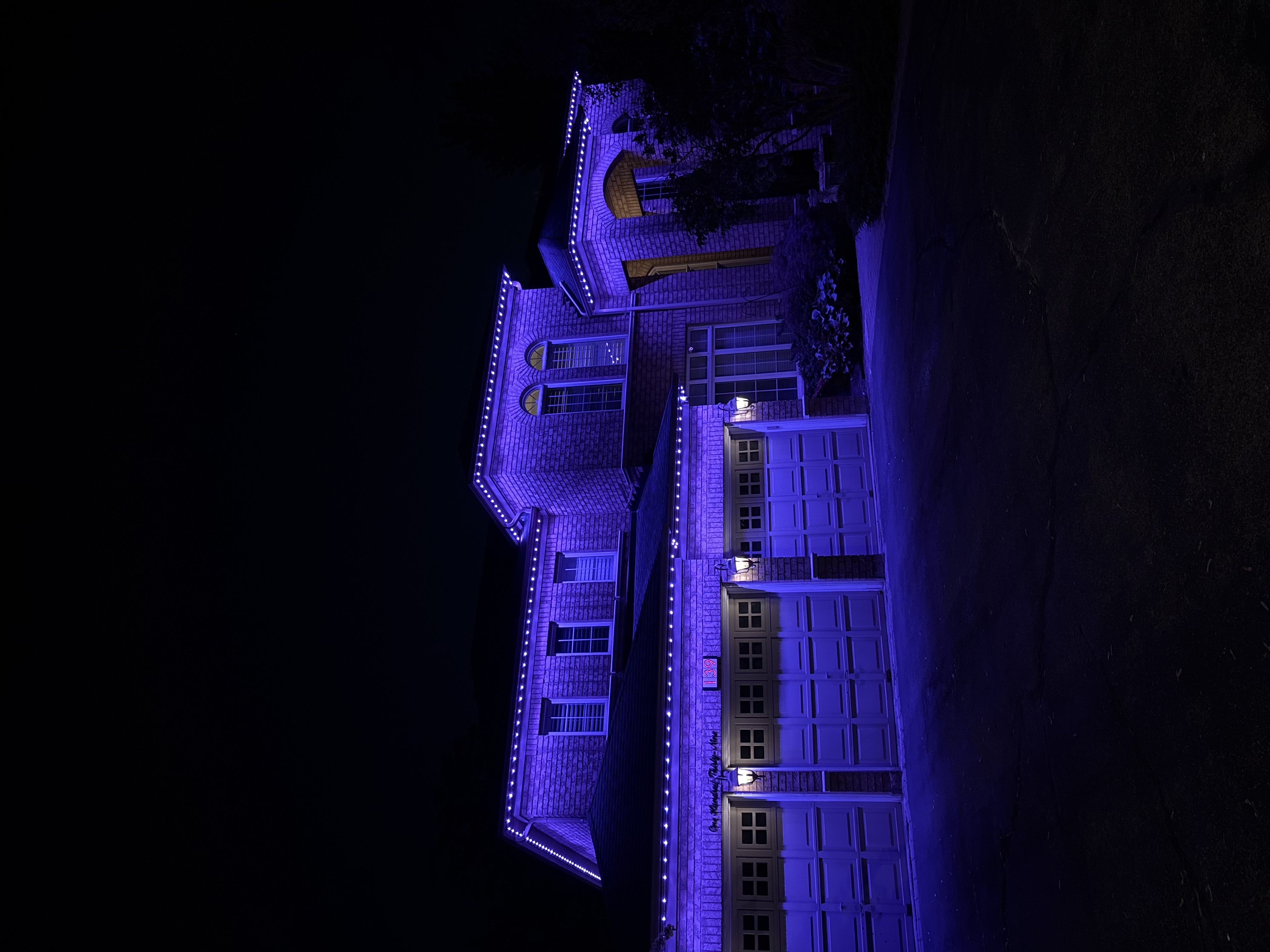 Purple permanent lighting along the roofline of a brick home