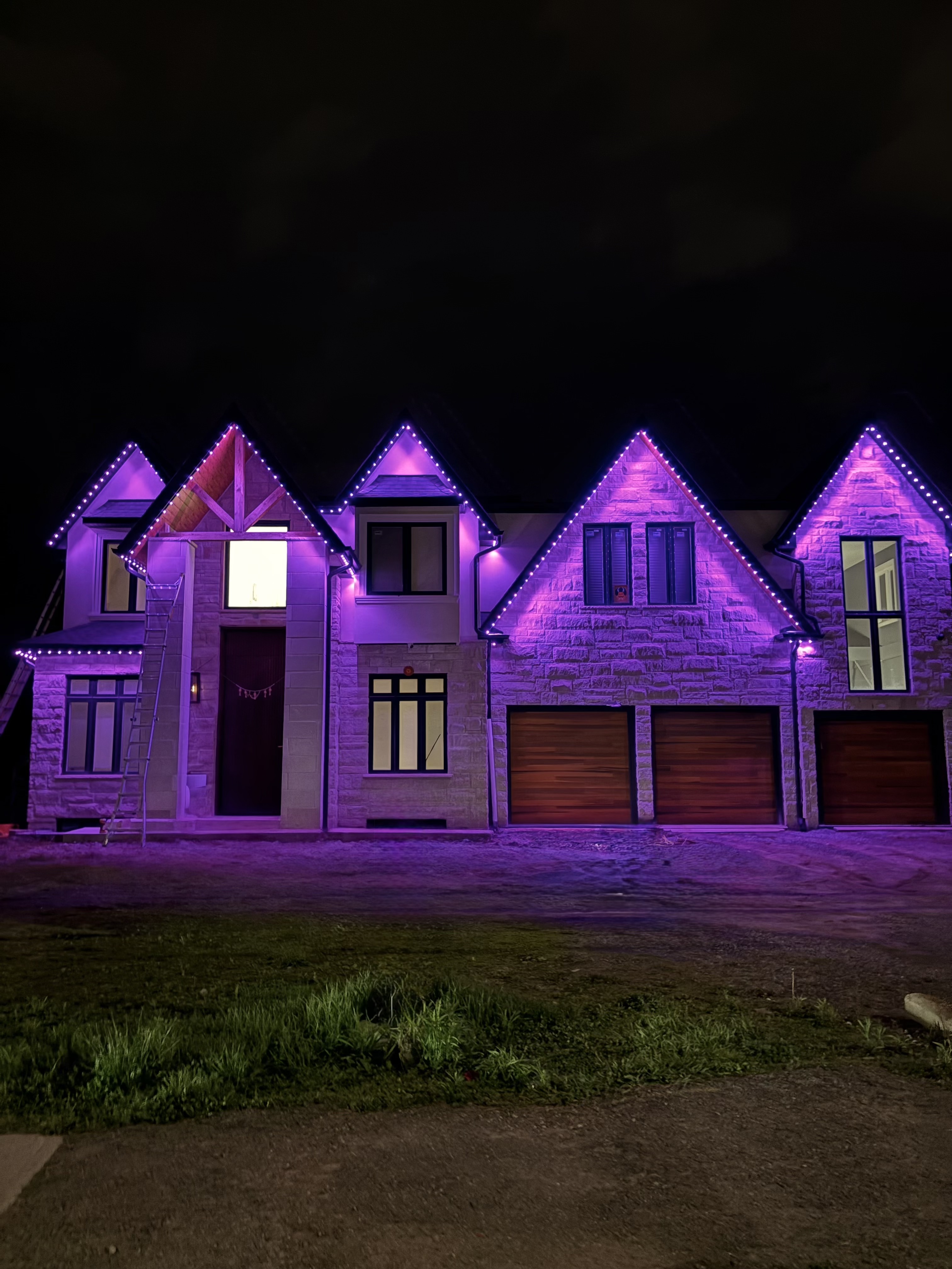Purple permanent lighting on the gables of a stone home