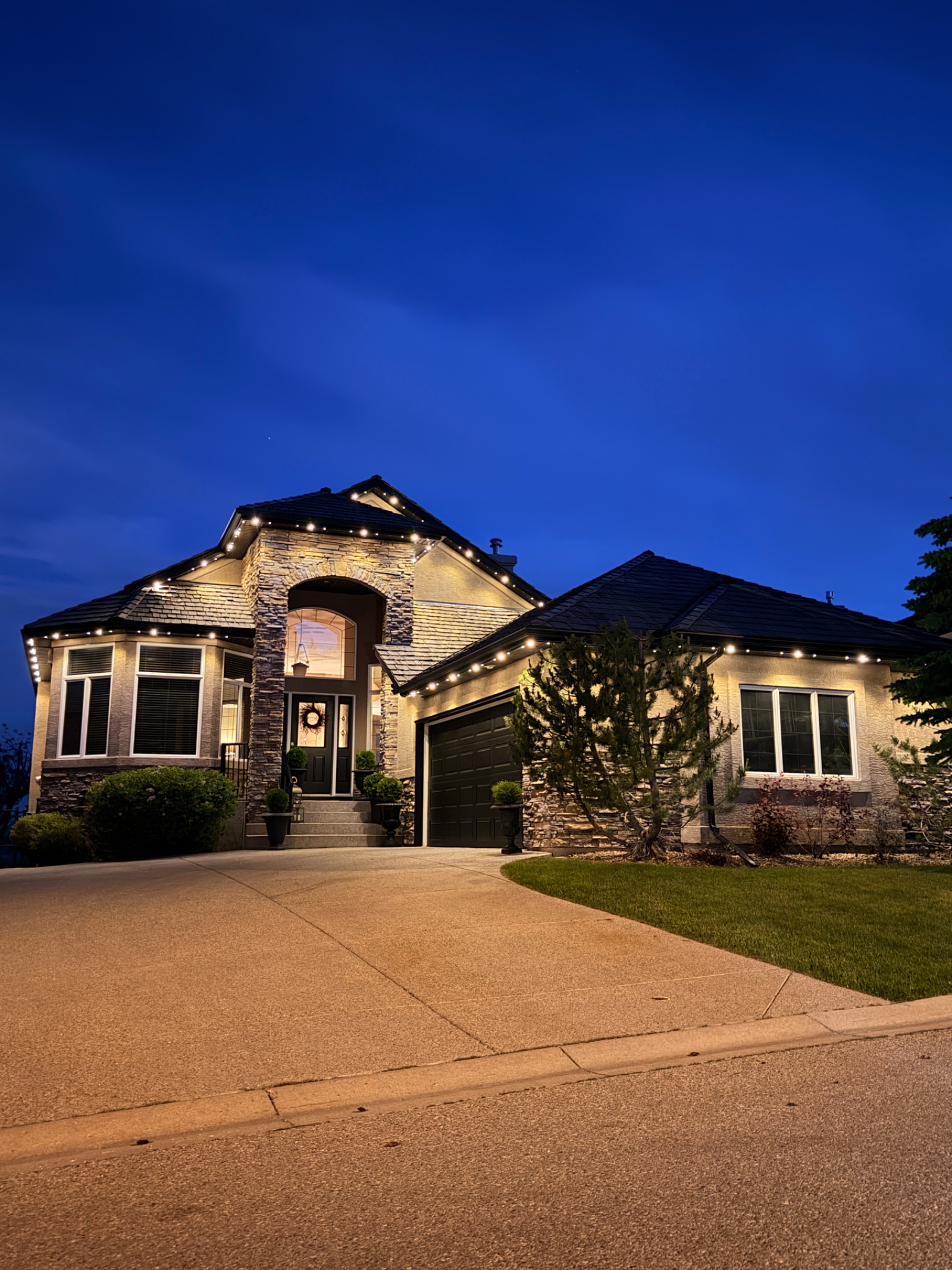 Warm white permanent lighting on a stone home at blue hour