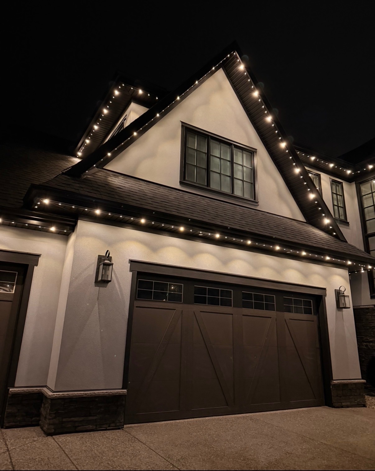 Warm white permanent lighting following the rooflines and garage of a modern home