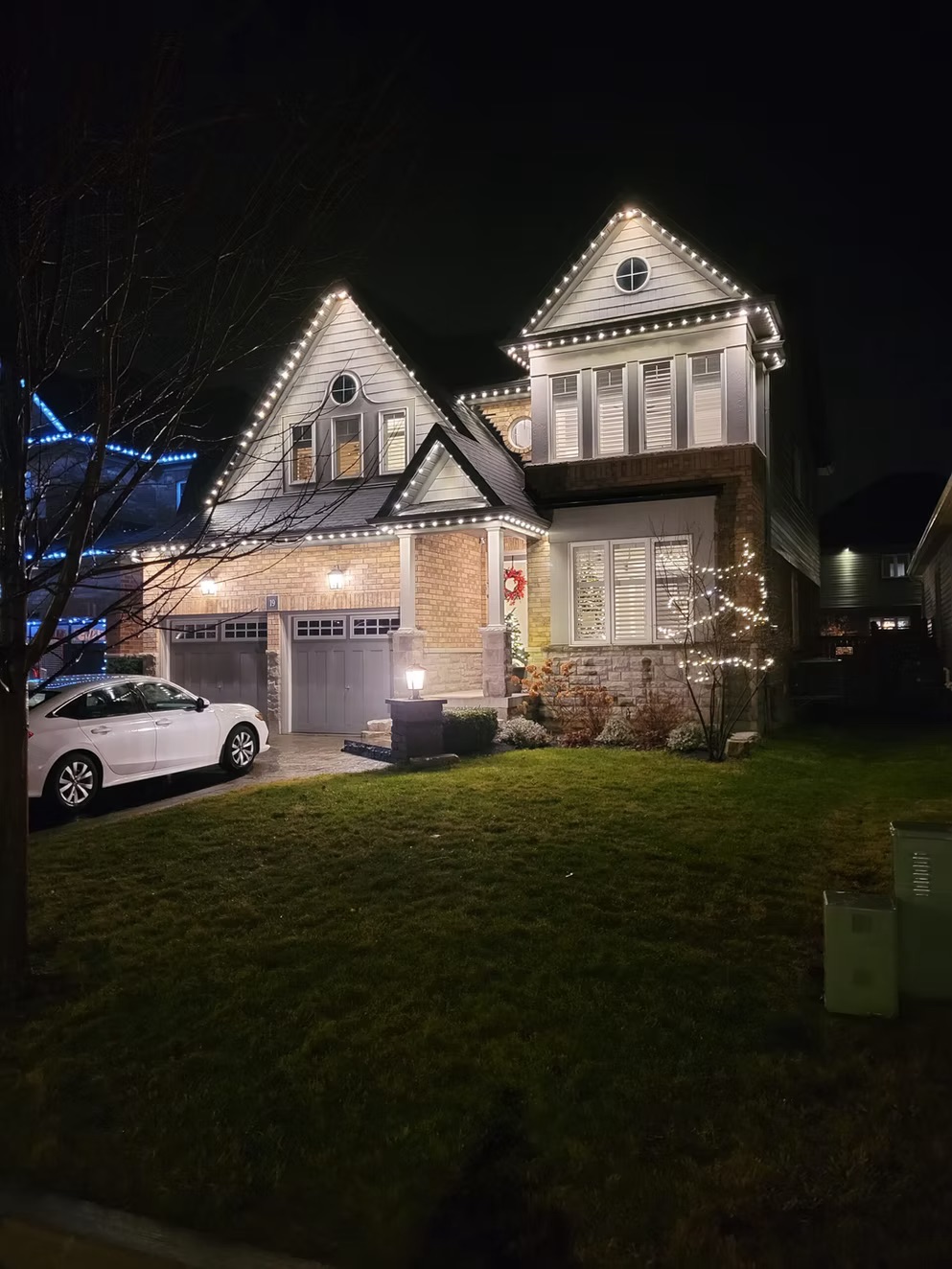 Warm white permanent lighting on a stone and siding home at night
