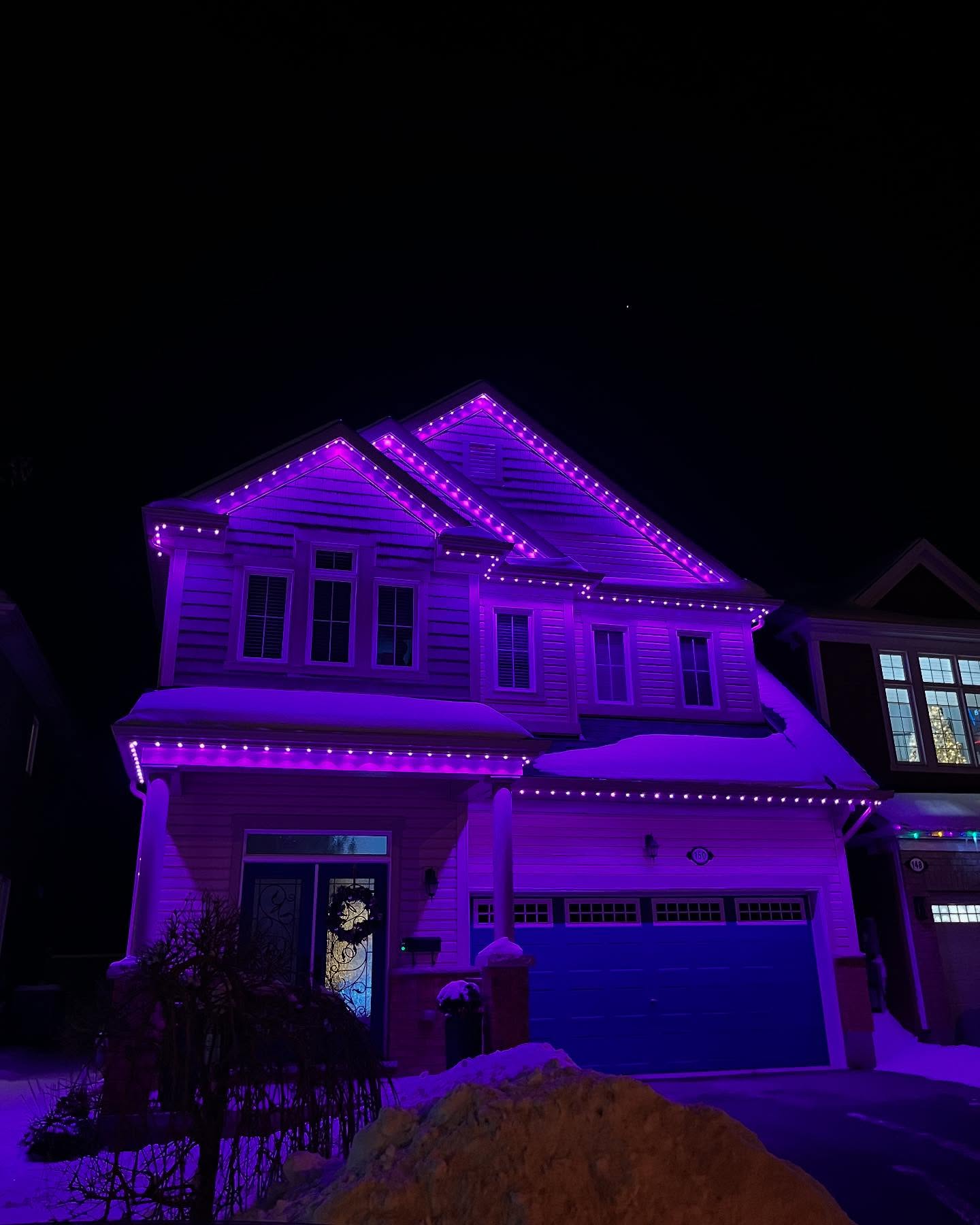 Purple permanent lighting across a two-storey home in winter