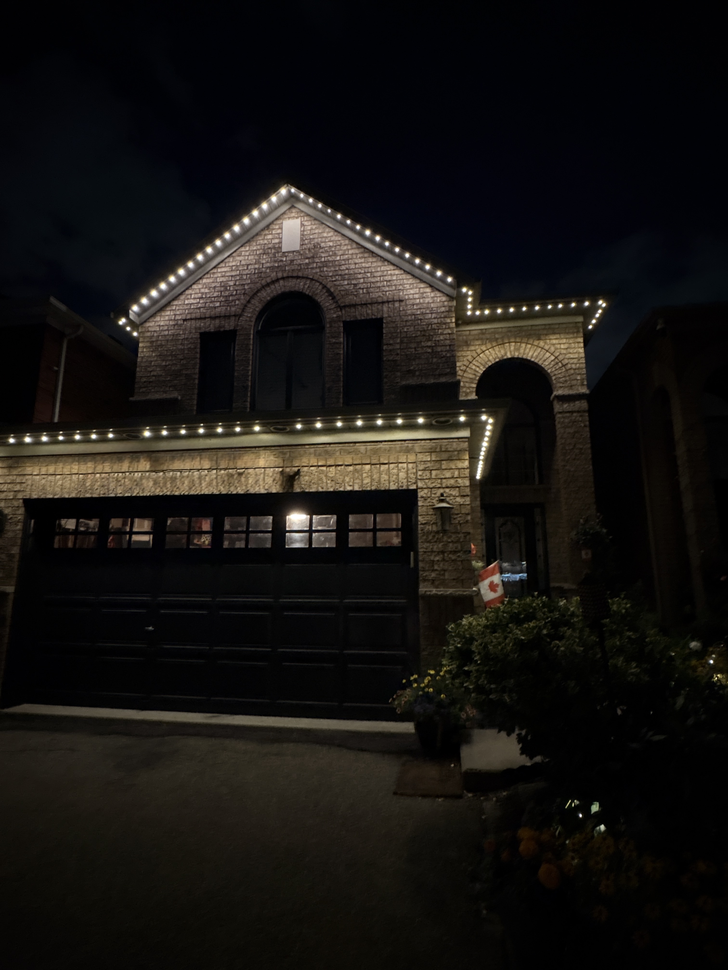Warm-white permanent LED lighting outlining the rooflines of a two-storey stone home at night.