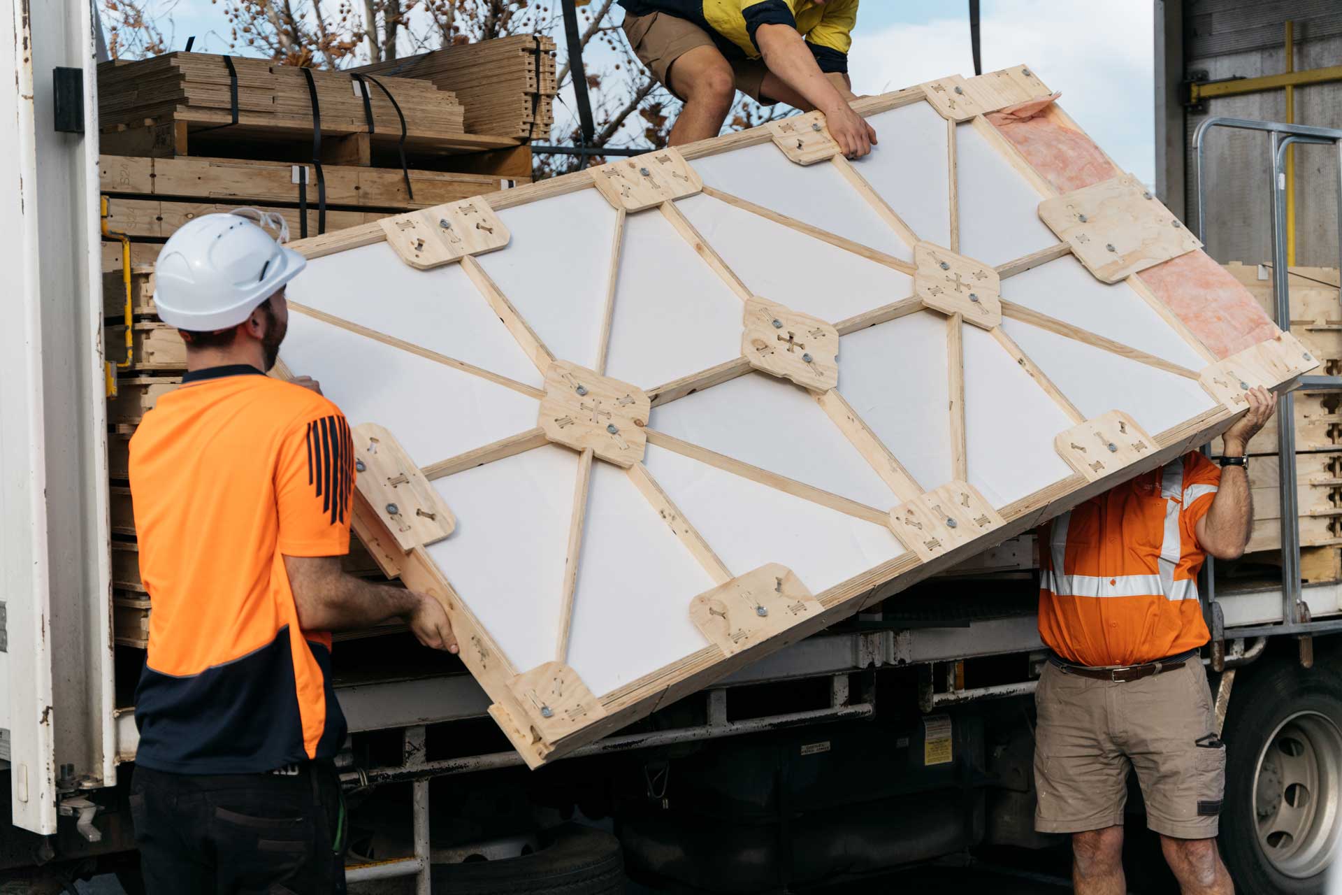 Three builders unloading an insulated XFrame panel out of a truck.