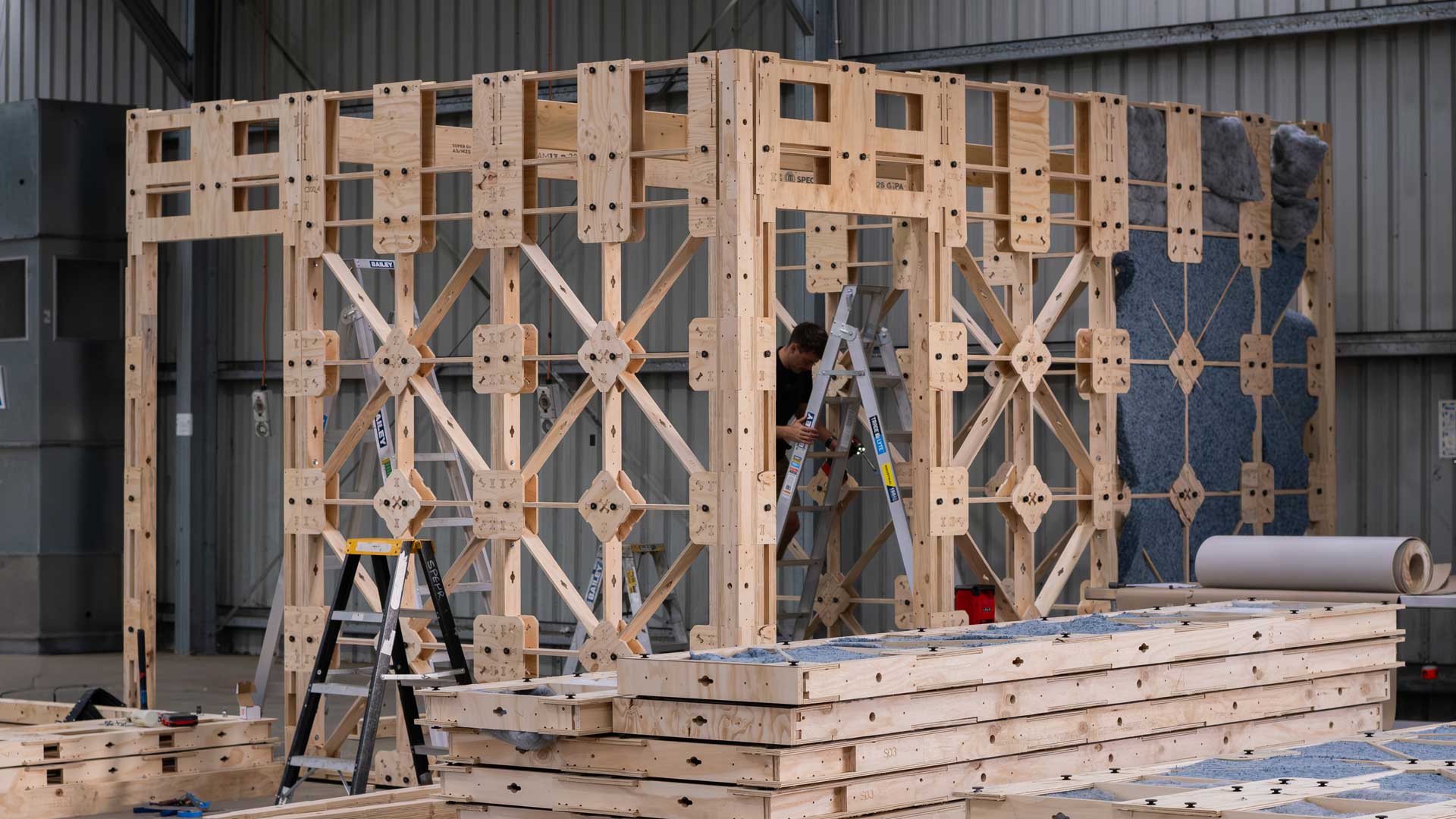 XFrame Panels in process of going up in a factory to form rooms, with preassembled frames in stacks in the front.
