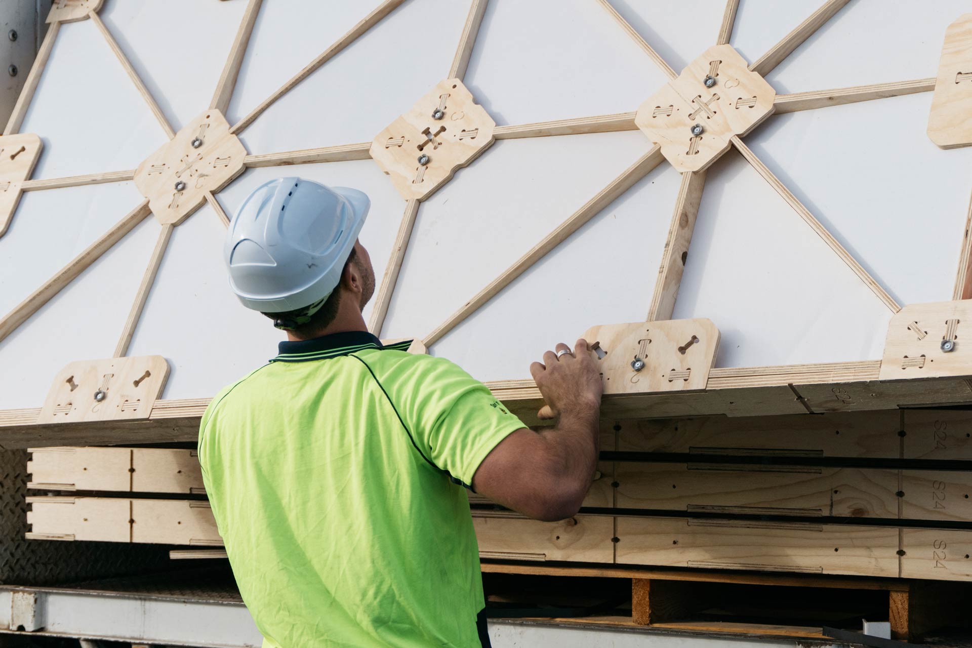 A builder wearing a yellow high visibility t shirt and white helmet unloading a preassembled XFrame panel out of a truck.