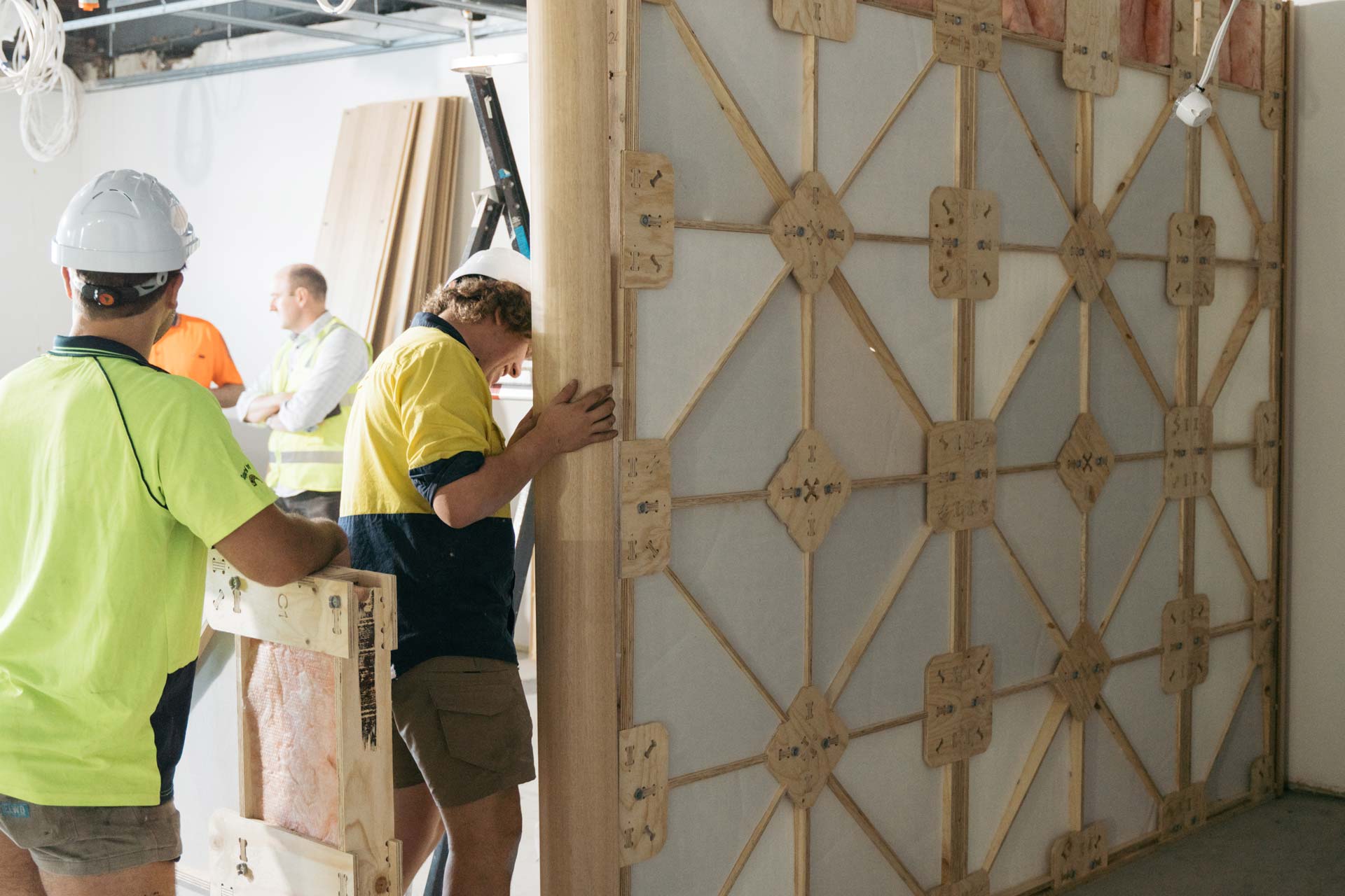 Four builders onsite with yellow high visibility t-shirt putting up preassembled XFrame panels in the construction site.
