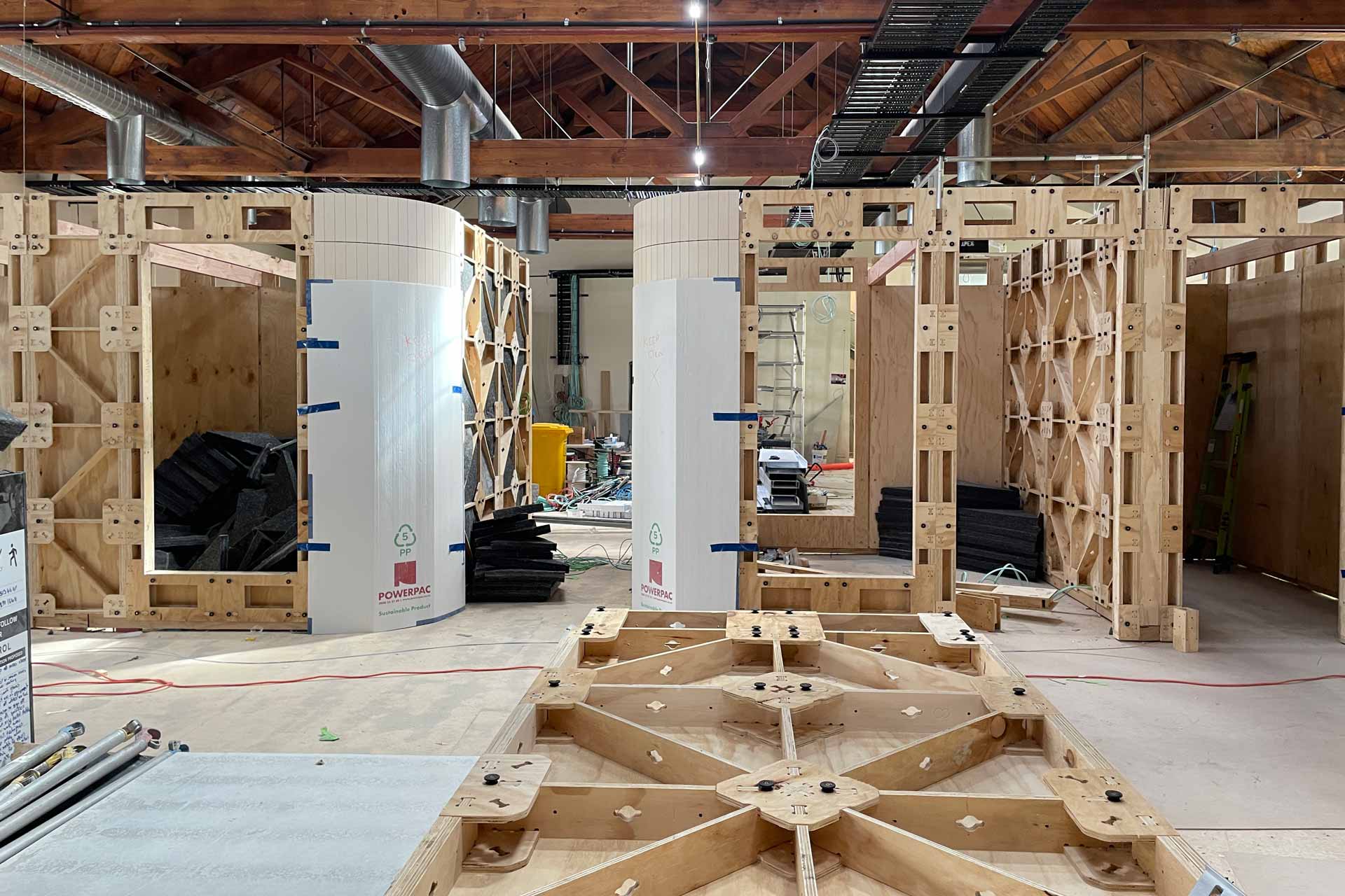 XFrame meeting rooms in the Meridian Energy office, during the construction stage, with bare XFrame panels up with the curved corners lined with wooden slat linings. A pile of preassembled XFrame panels are in a pile in the foreground as well.