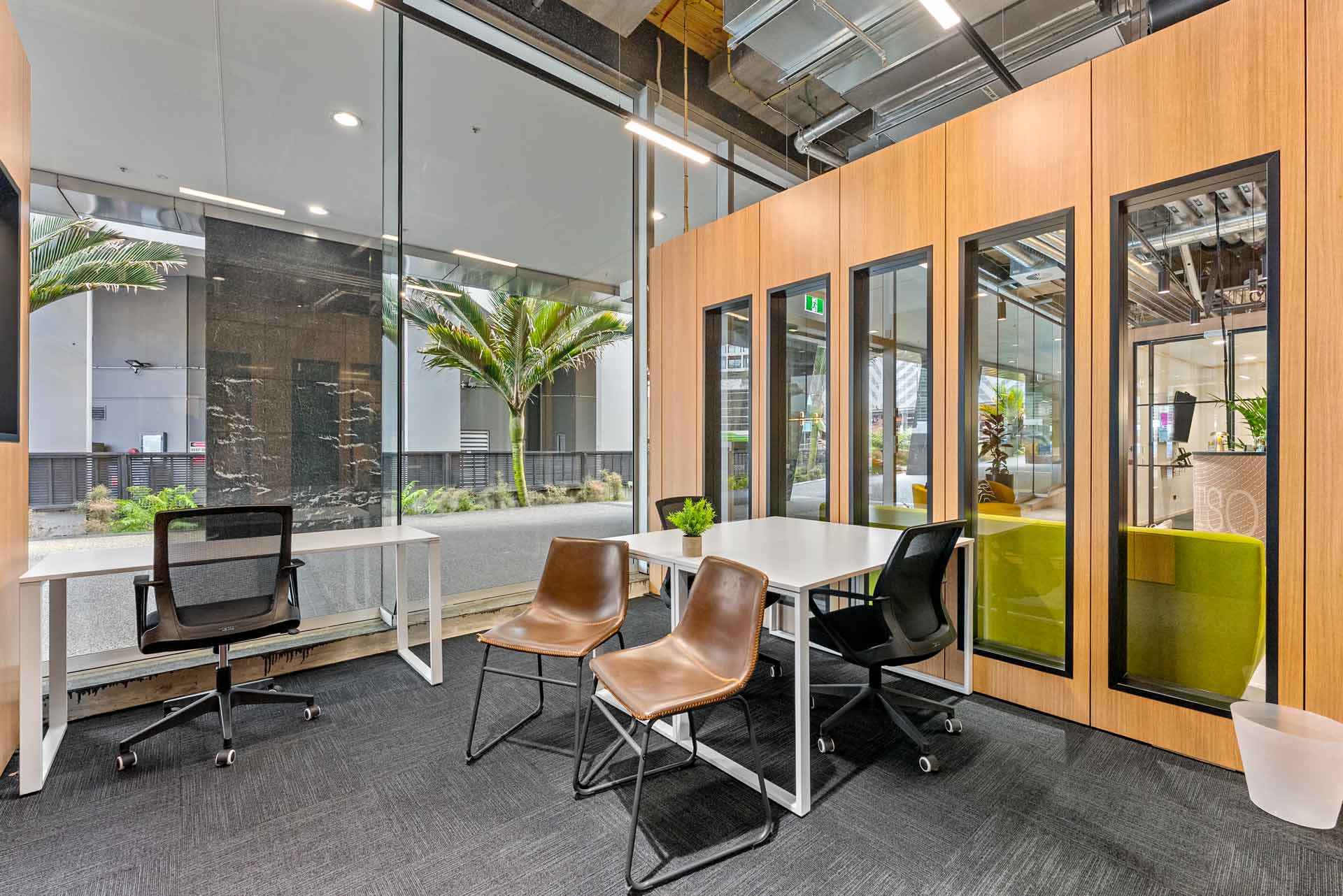 Inside a meeting room in WOTSO Te Toangaroa, with windows looking outside, with two desks and lots of chairs.