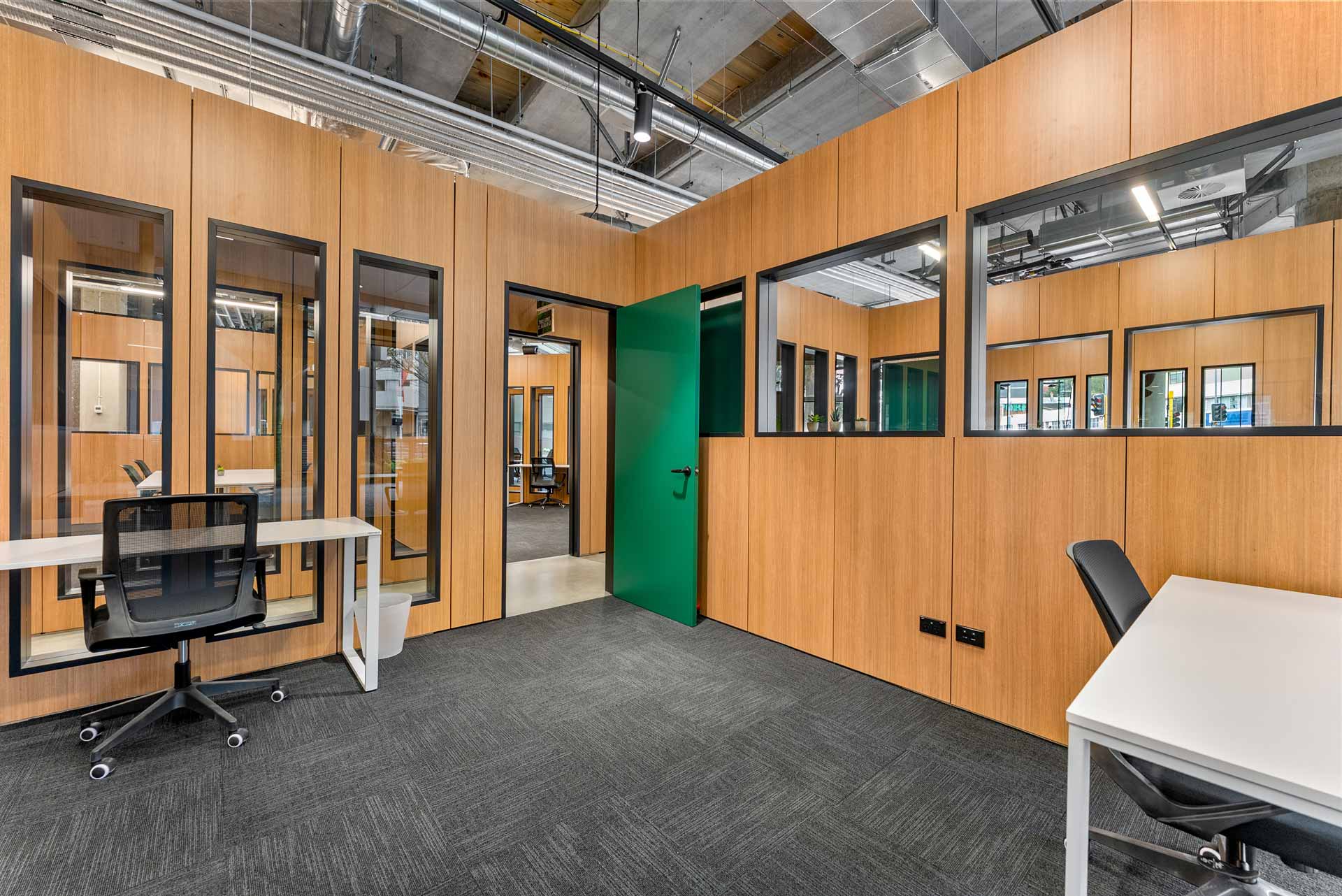 Wotso Te Toangaroa flexible co-working rooms made out of XFrame with bright green doors, and some white desks and black office chairs.