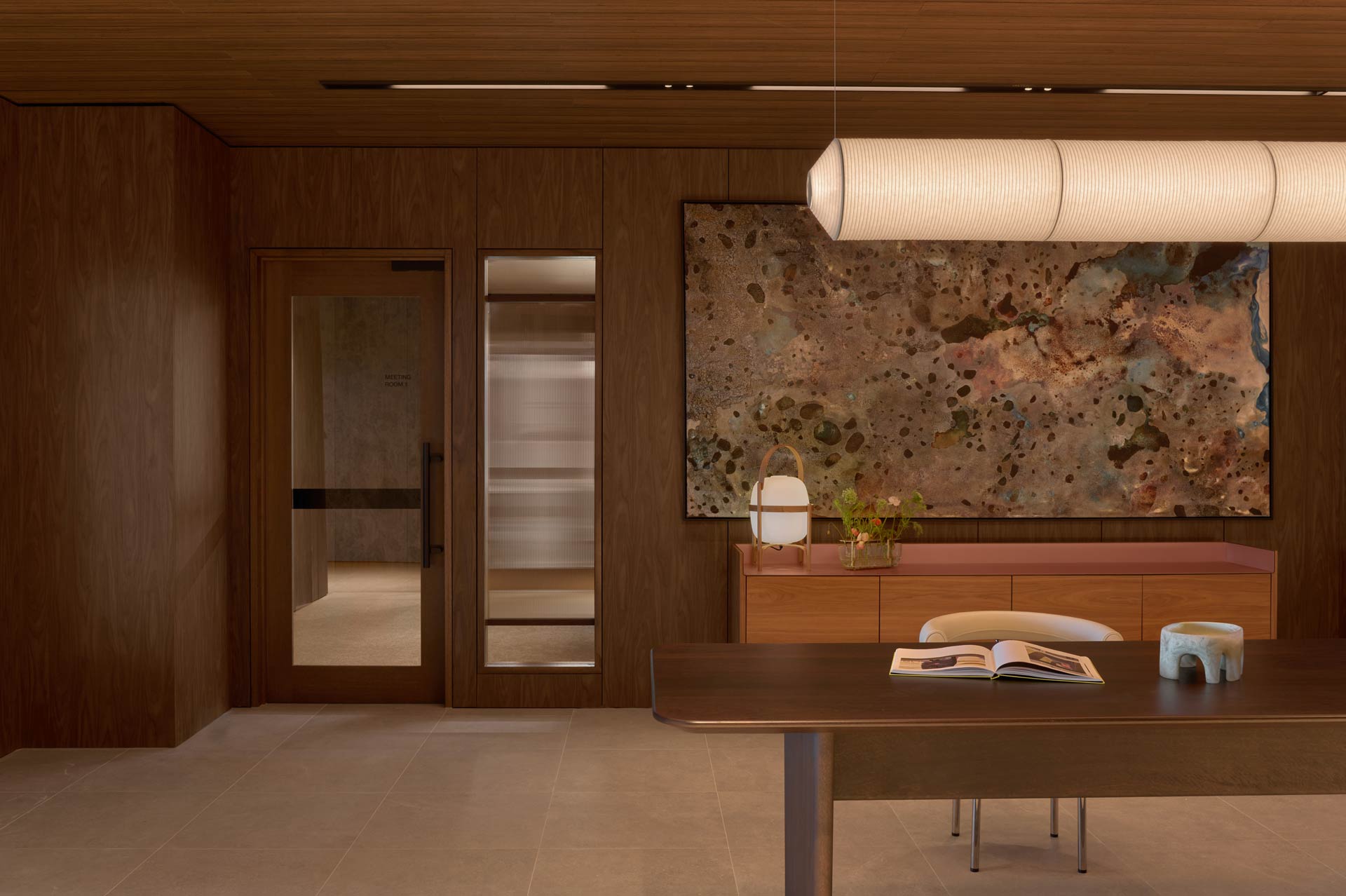 The reception area of Westralia Square 2, with Walnut lining walls, a walnute desk in the foreground with a large marble picture frame in the back and one large tube lantern line hanging from the ceiling.