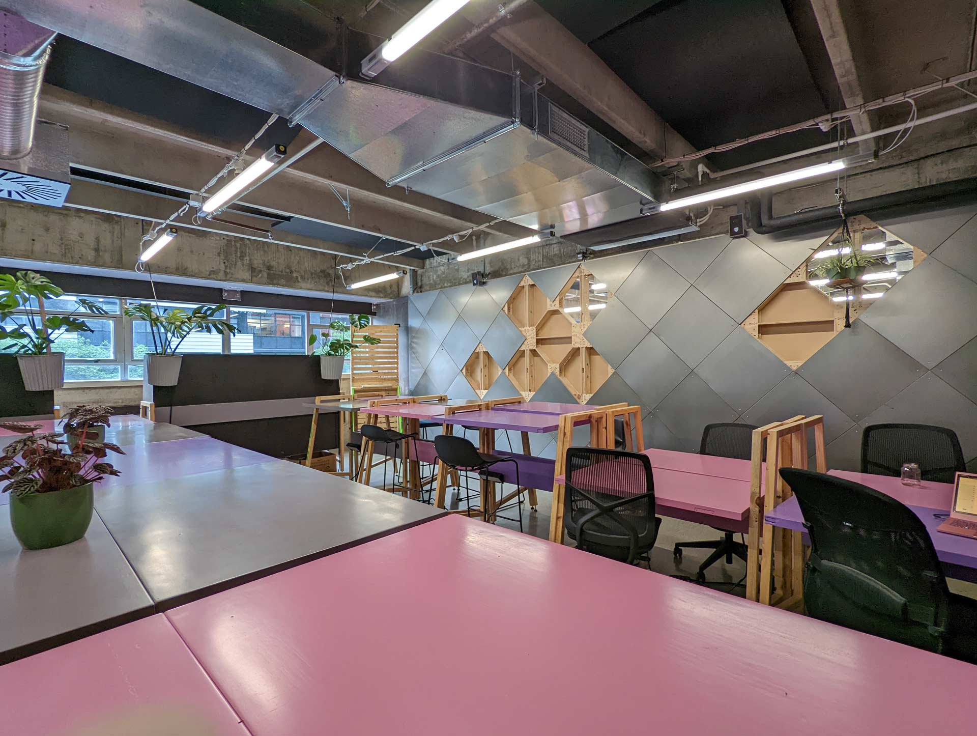Long XFrame demountable partition with powder coated sheet metal wall linings in 600mm square diamonds, separating a large room, with prink and grey, hight and low desks. and some plants.