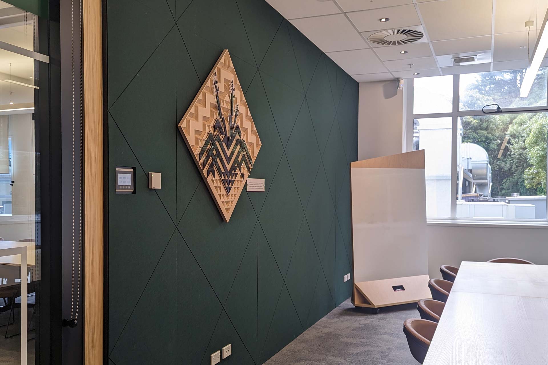 3m high panels, adorned with 12mm Autex PET linings (with a grooved face pattern) inside a meeting room, with a long board desk with chairs and a moveable whiteboard on wheels.