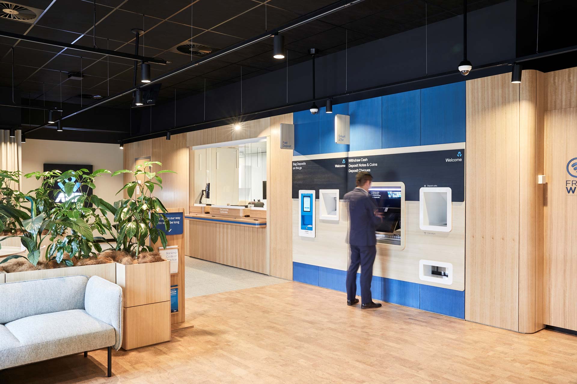 Inside of ANZ Springvale, with a man in a suit using an ANZ Smart ATM made our of XFrame Wall Linings, and a teller window to the left.