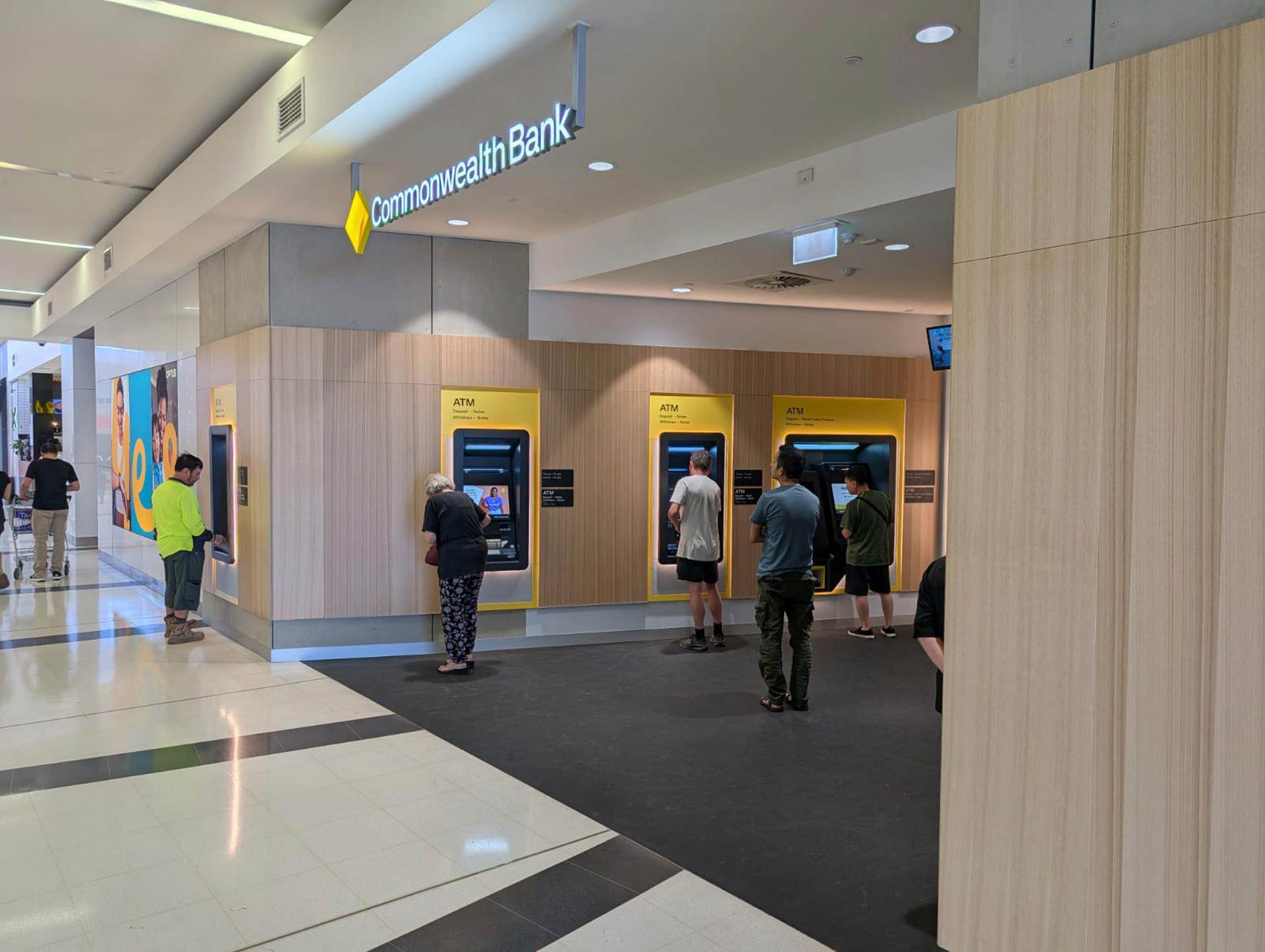 Commonwealth Bank ATMS in a shopping wall with customers using them,