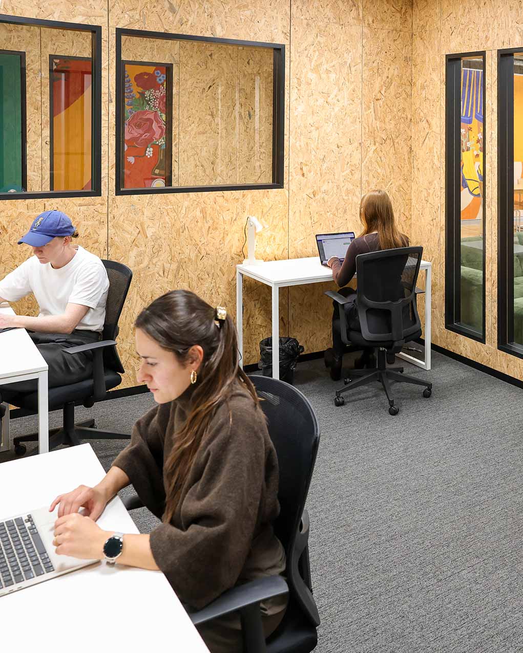 Three people working at individual desks inside an XFrame office with timber panel walls and internal windows.