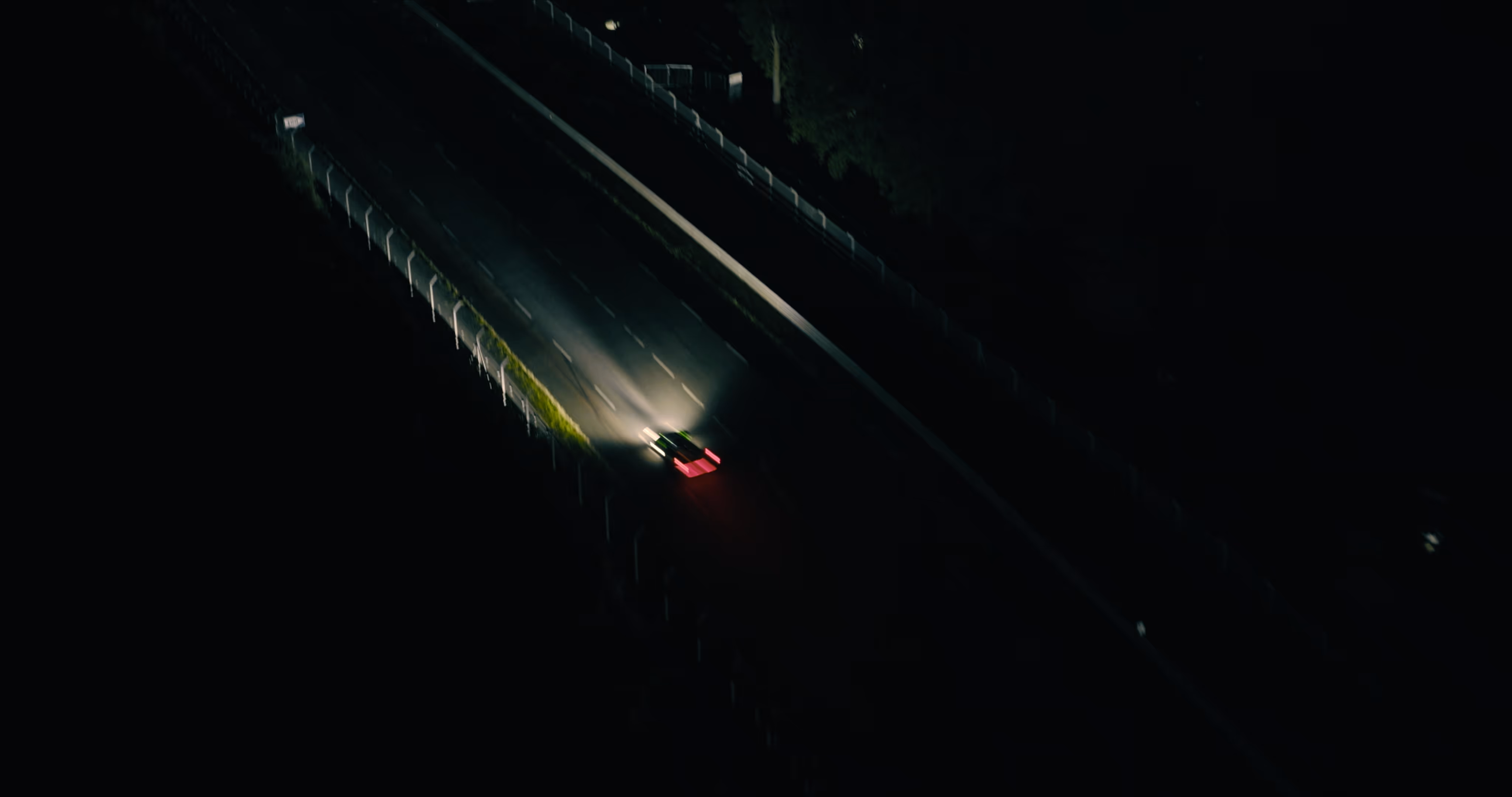 A car with headlights and red taillights driving on a dark, empty highway at night - 2DIE4 Film