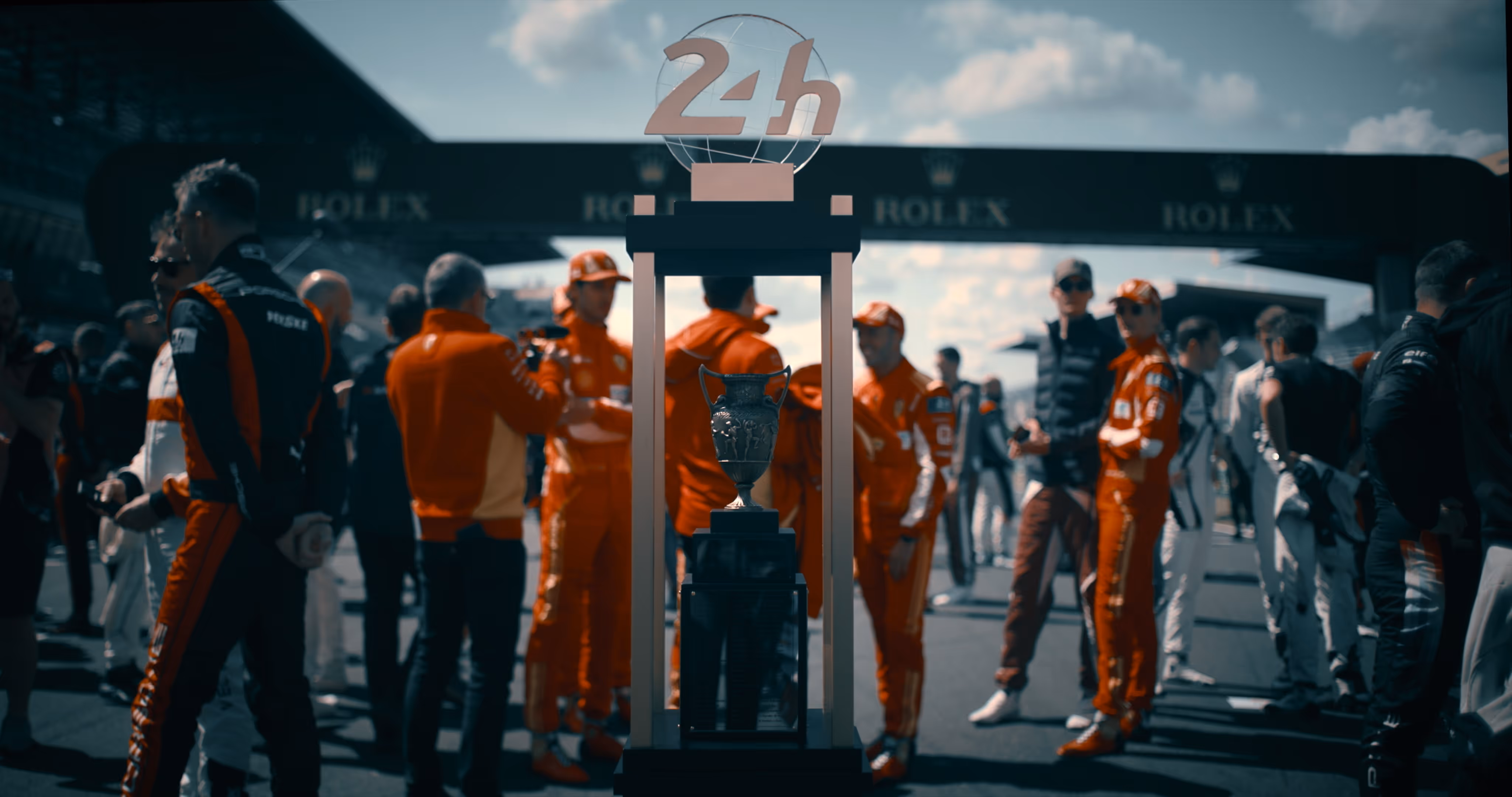 Trophy displayed in front of a group of race car drivers wearing orange uniforms on a race track.