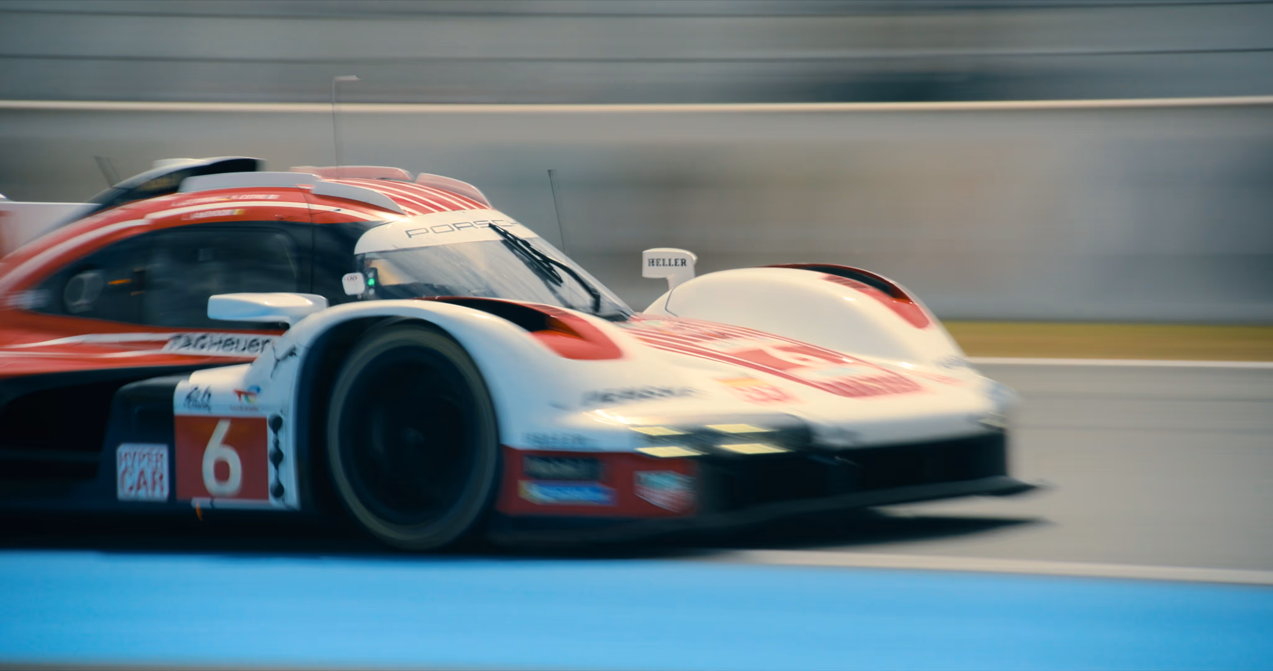 White and red Porsche racing car number 6 speeding on a track with blurred background.