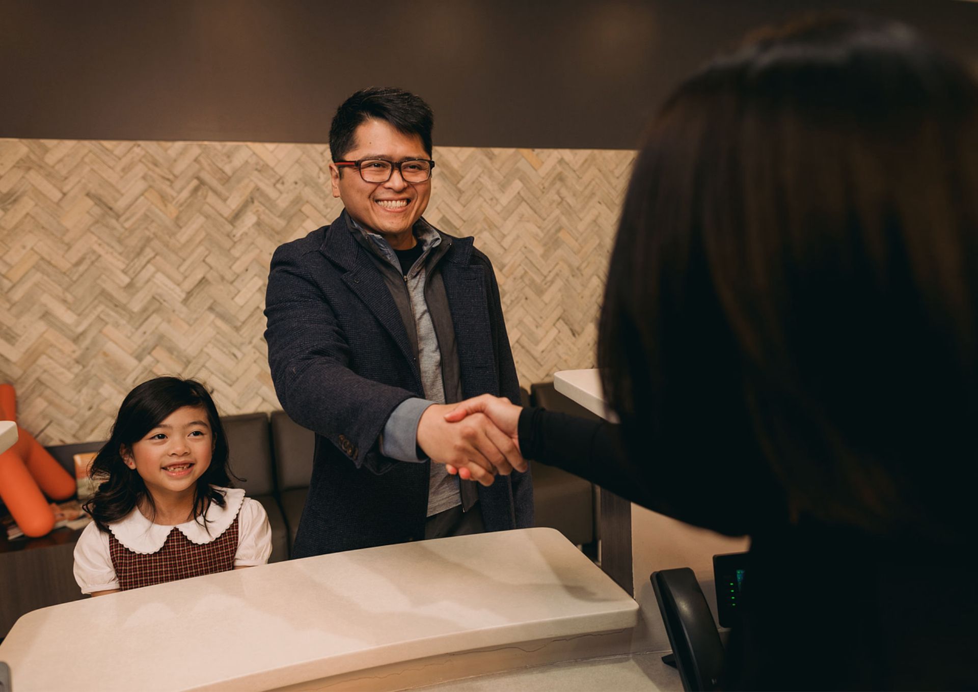 Smiling man shaking hands with a woman while a young girl looks on in a reception area.