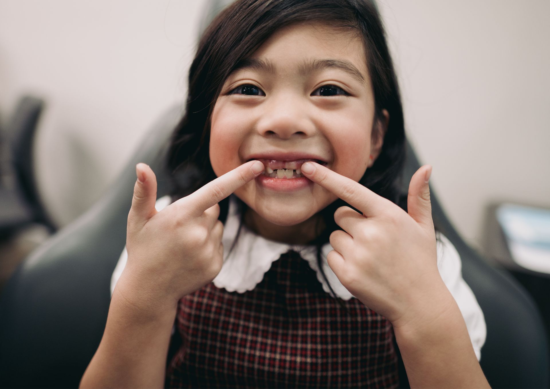 Smiling young girl showing two missing front teeth while pointing at her mouth.